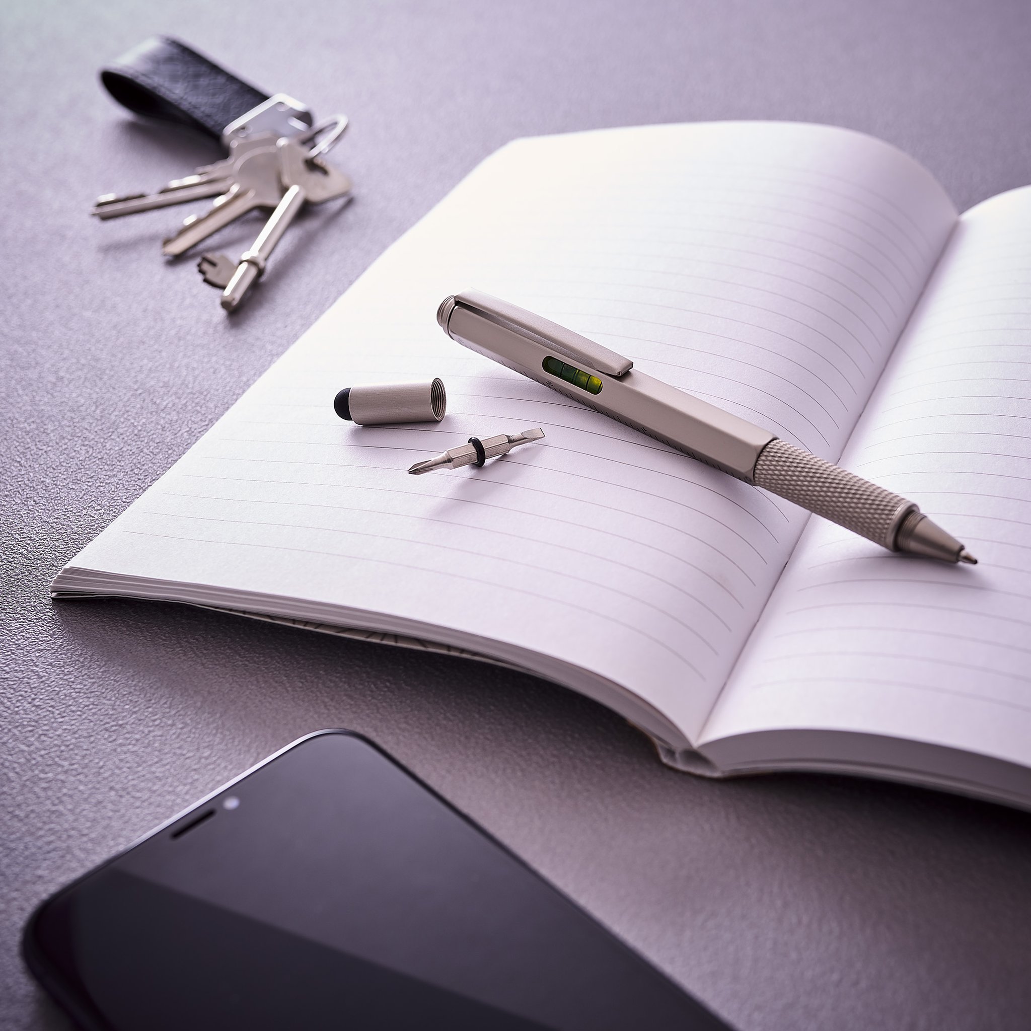Stylo Multi-Outils 6-en-1 sur un carnet ouvert, avec son embout de tournevis, des clés et un téléphone