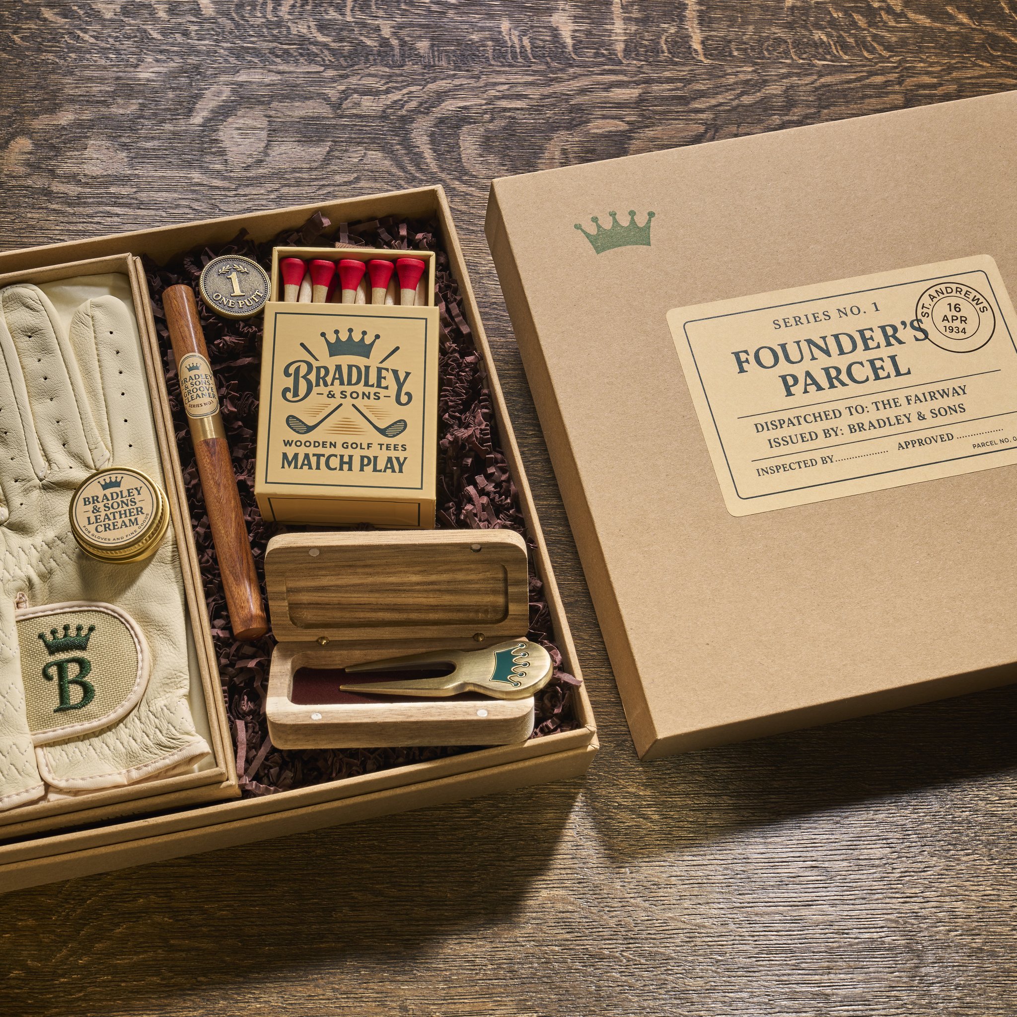 Geöffnete Golf-Geschenkbox Founder's Parcel mit Lederhandschuh, Tee-Schachtel und Divot-Tool im Holzetui
