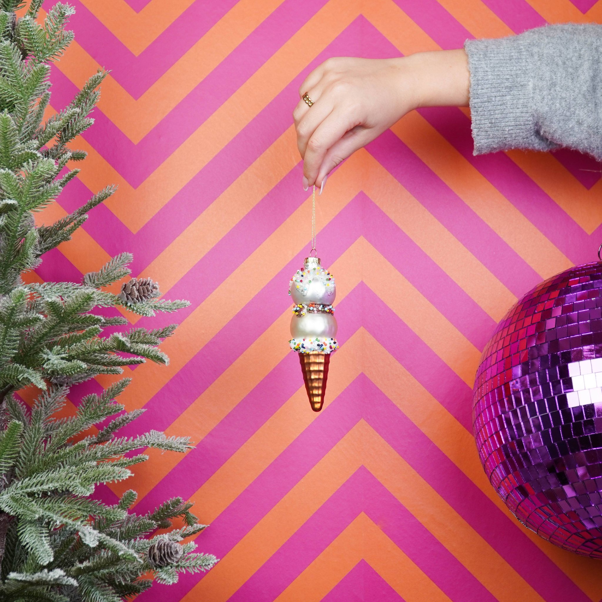 Glacé Weihnachtsanhänger in Rosa-Weiss wird vor pinkem Chevron-Hintergrund gehalten