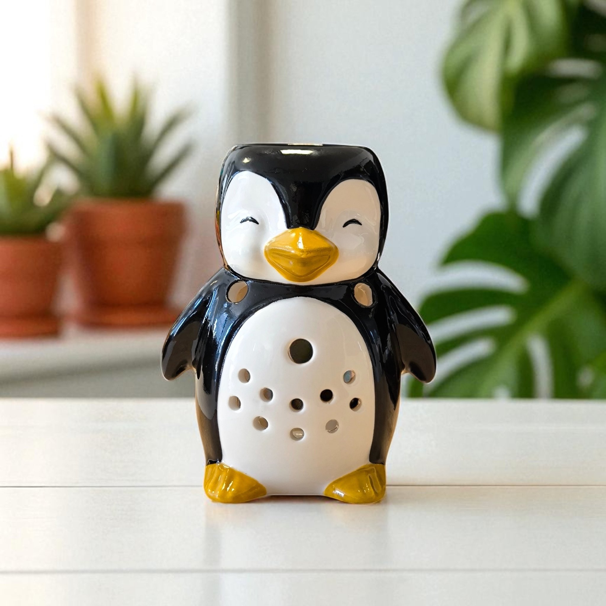 Pinguin-Duftlampe auf hellem Regal mit Grünpflanzen