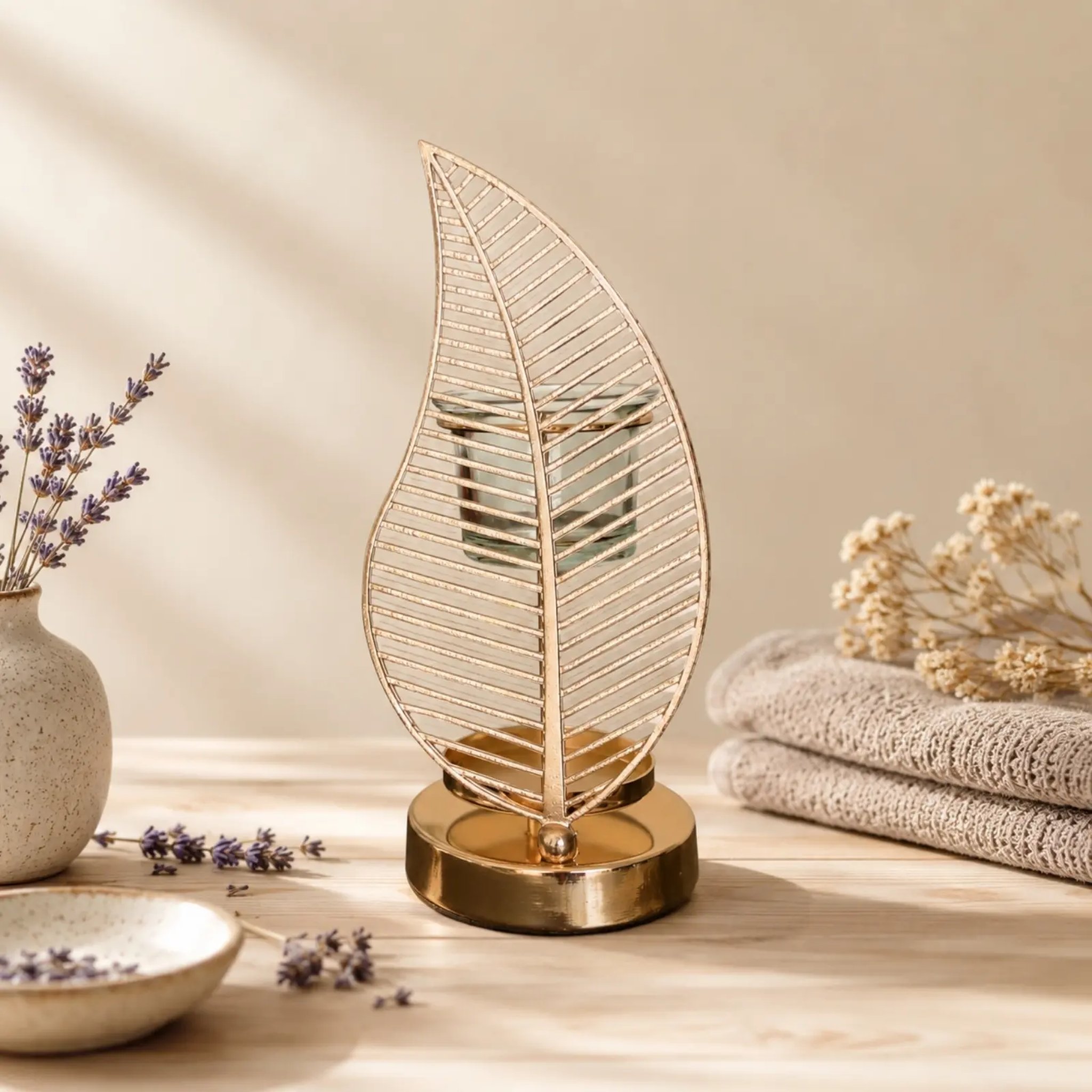Palm leaf oil burner with gold-coloured base beside lavender and towels