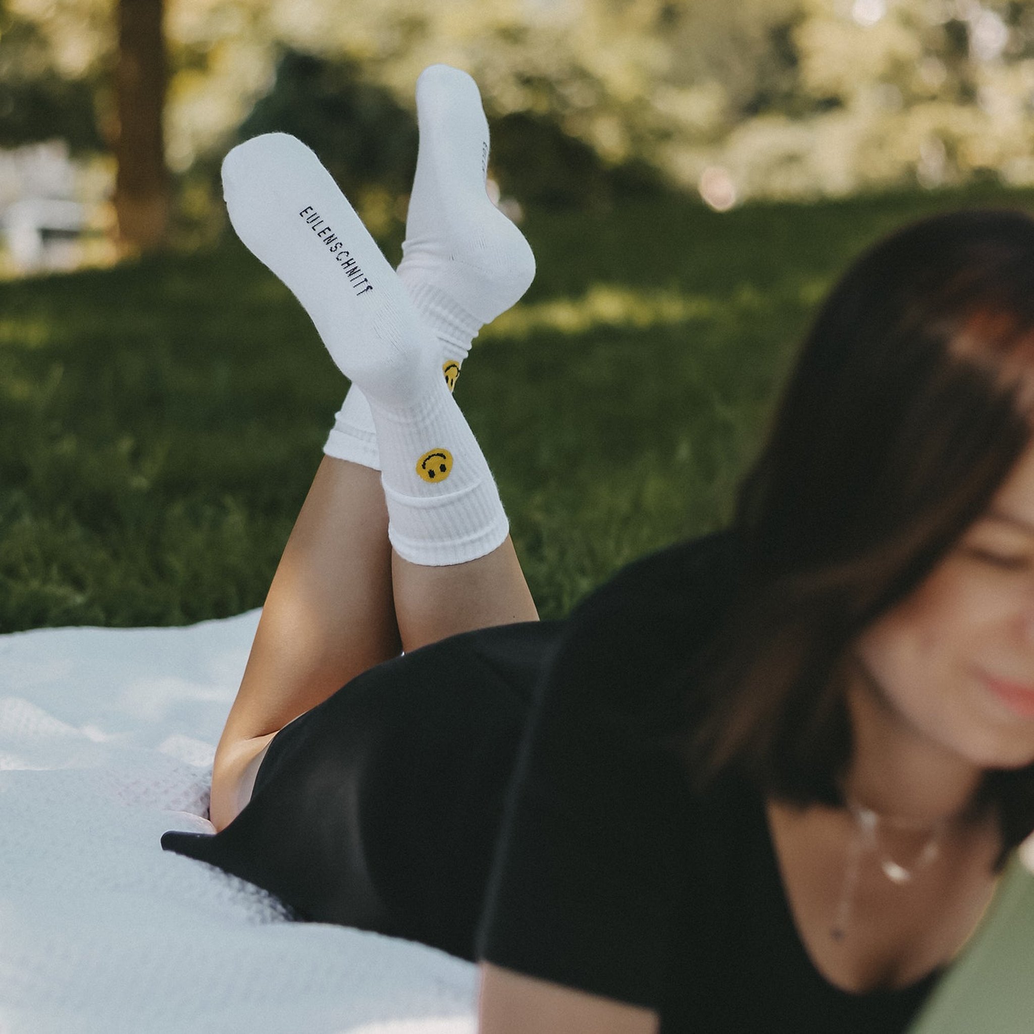 Lachende Frau auf einer Decke im Park mit den Smiley-Socken an den Füssen