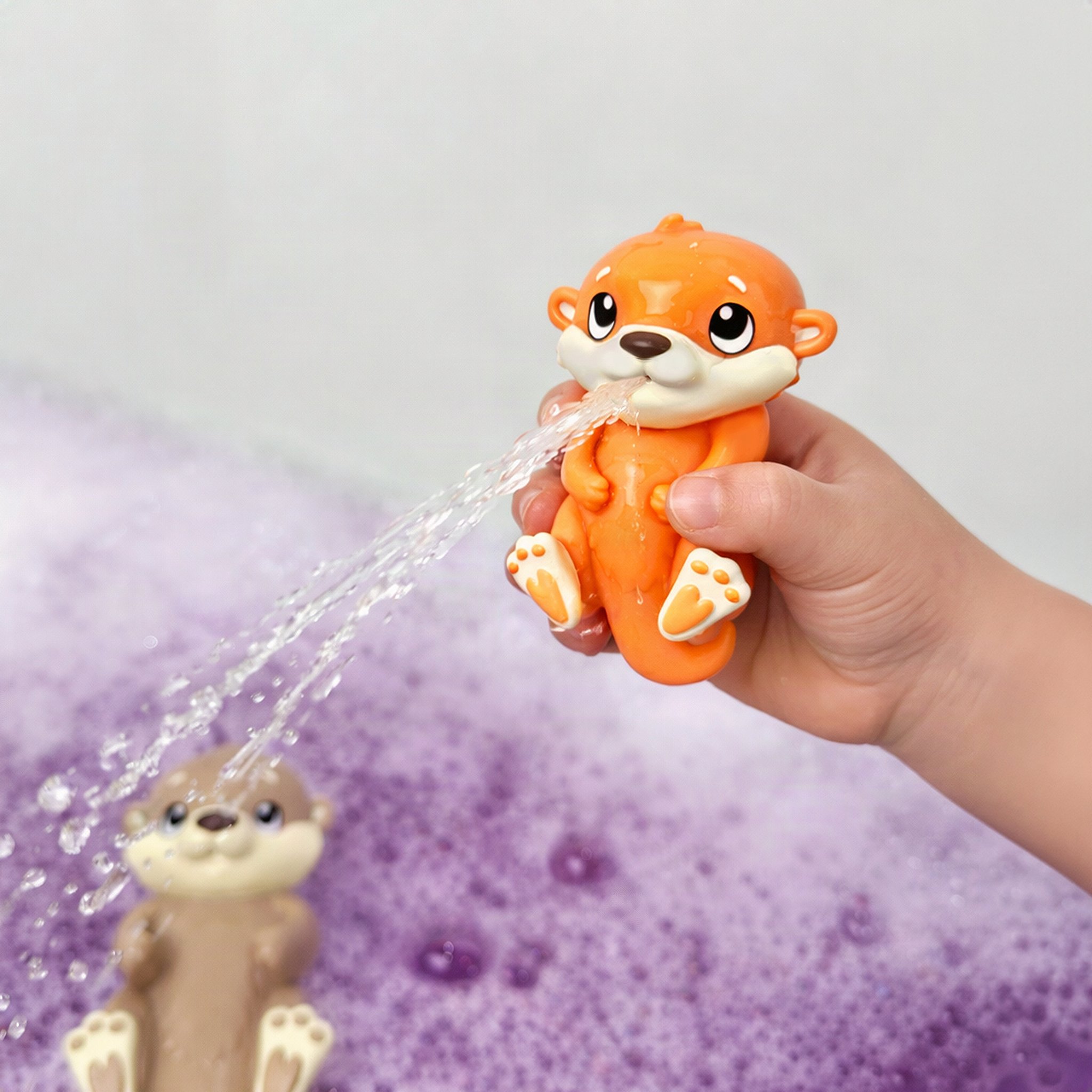 Child's hand squeezing the orange baby otter as it squirts a jet of water