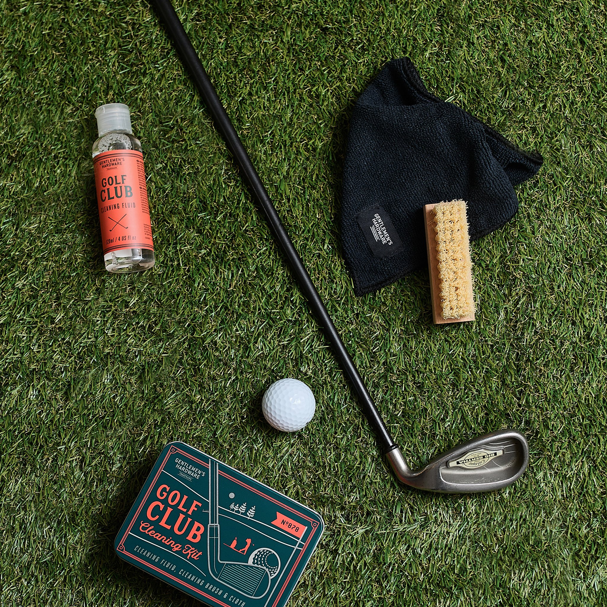 Golf club, ball, bottle, brush and cloth of the cleaning set on artificial turf, with the tin at the bottom