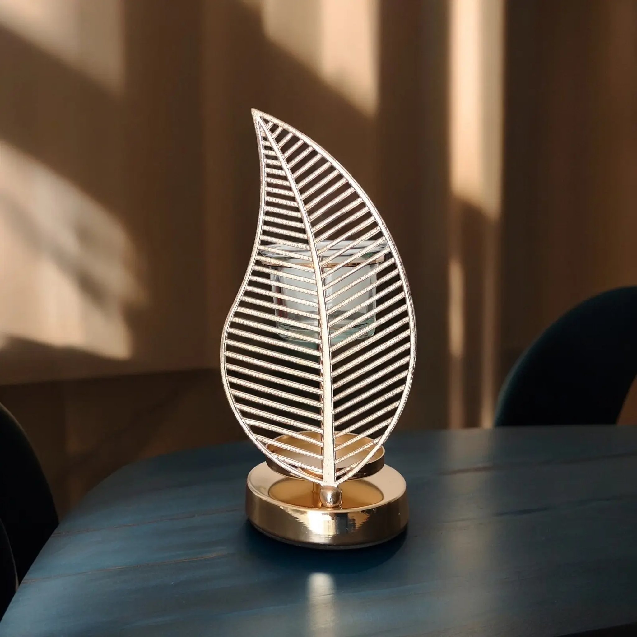 Palm leaf oil burner made of metal ribs with glass cup in window light and shadow