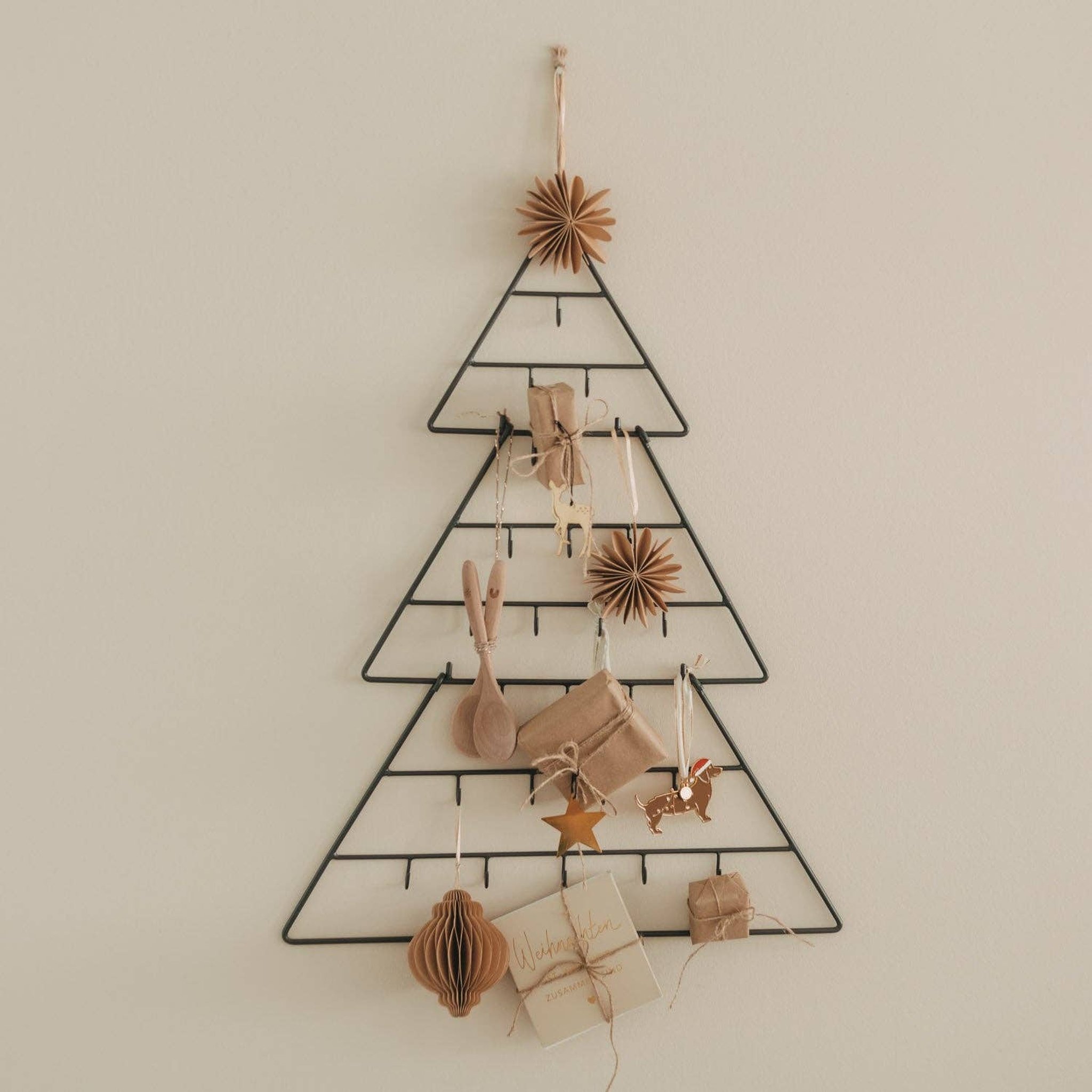 Adventskalender Tanne aus schwarzem Metall an einer hellen Wand, dekoriert mit kleinen Päckchen und Anhängern