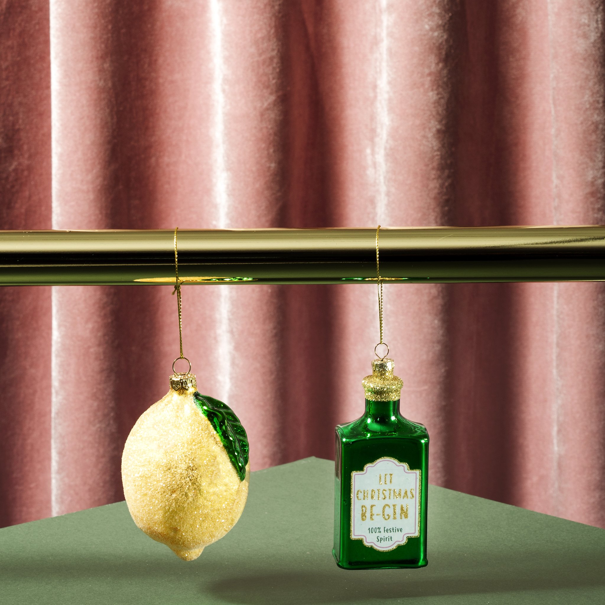 Weihnachtsschmuck Zitrone hängend neben Gin-Flaschen-Anhänger vor rosa Samt