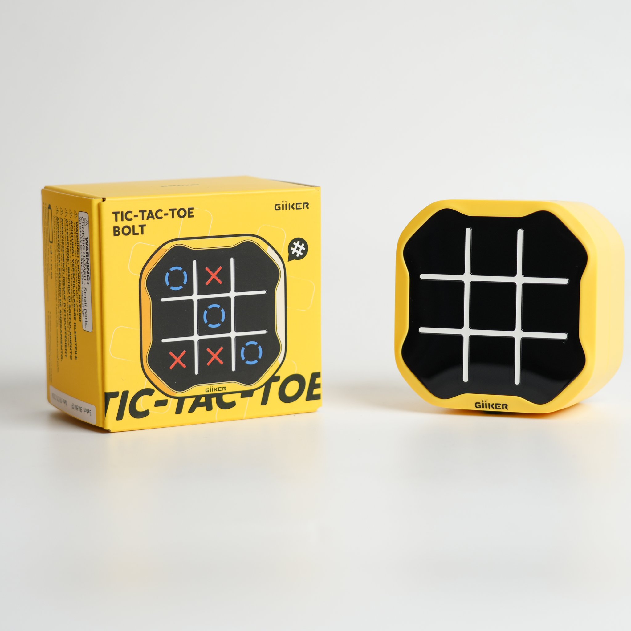 Console Tic Tac Toe à côté de son emballage jaune, photo studio sur fond neutre.