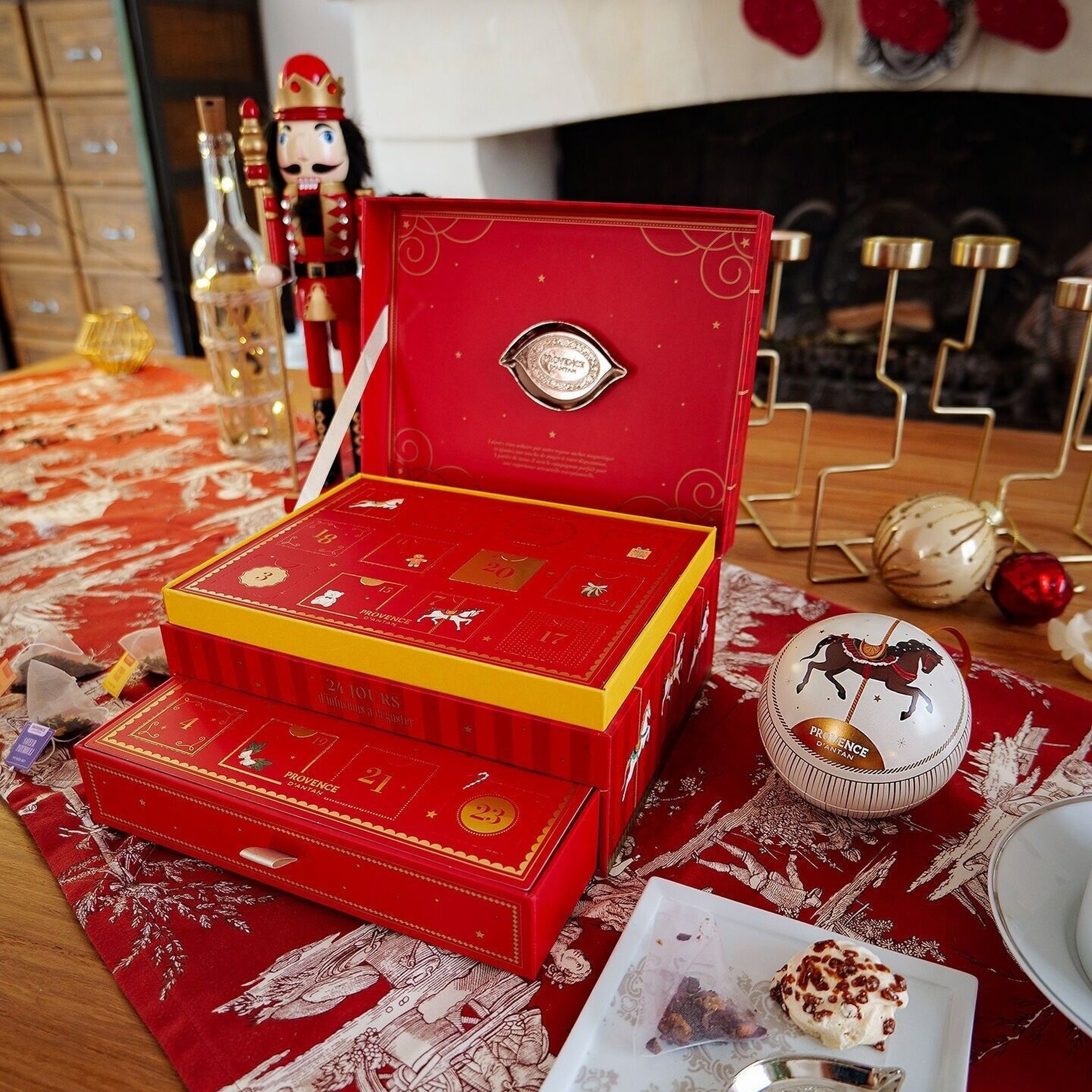 Geöffneter Tee-Adventskalender auf dem Tisch vor dem Kamin, daneben Nussknacker und Teekugel