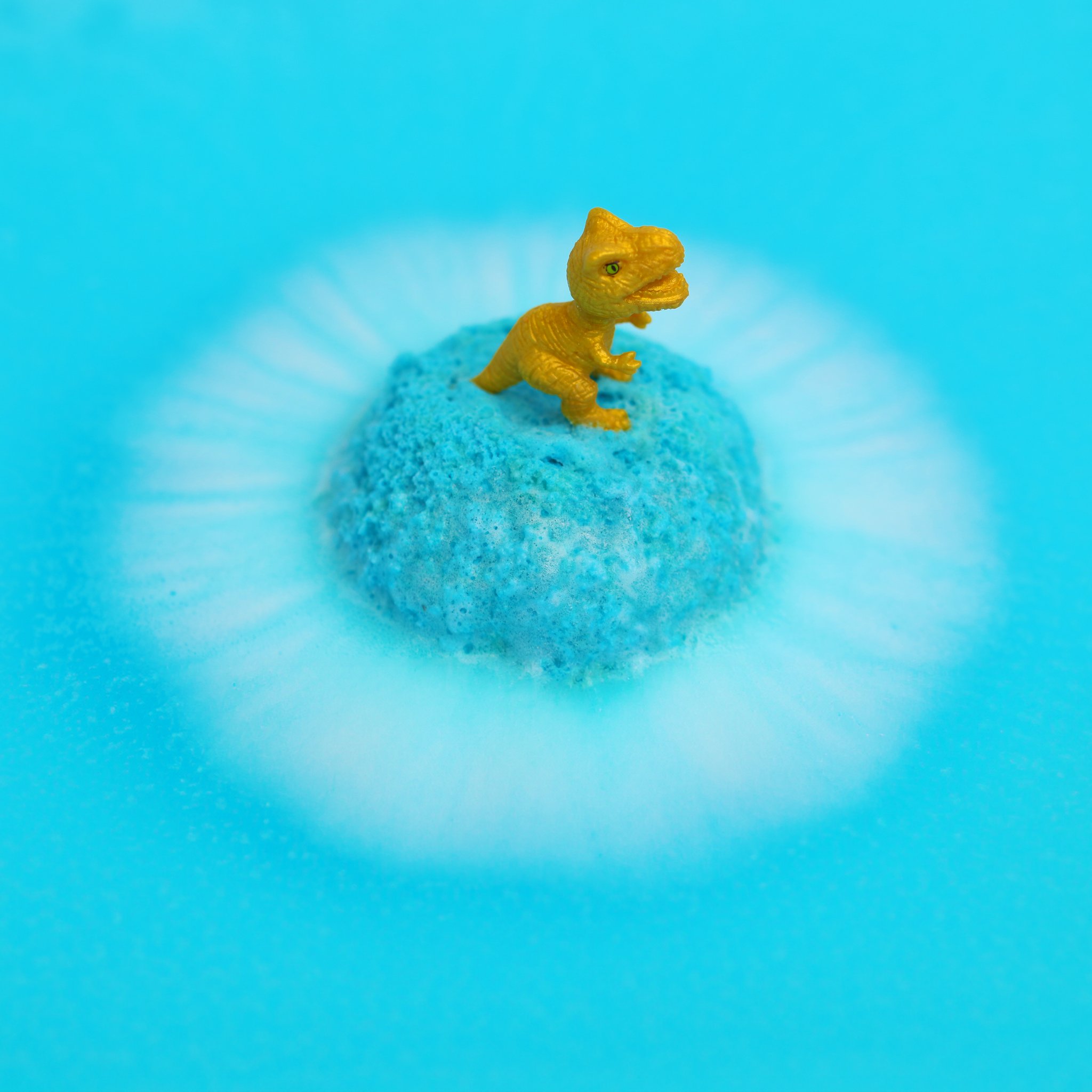 Golden dino figure on a fizzing blue bath bomb
