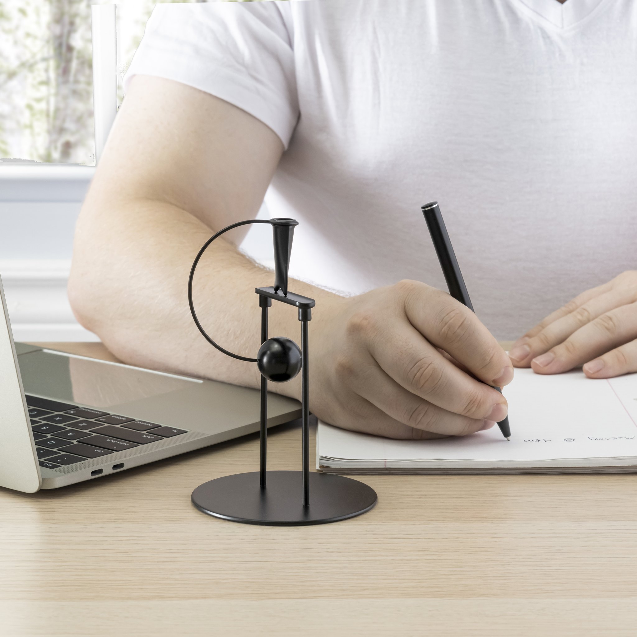 Penna in equilibrio sulla scrivania accanto a laptop e blocco note