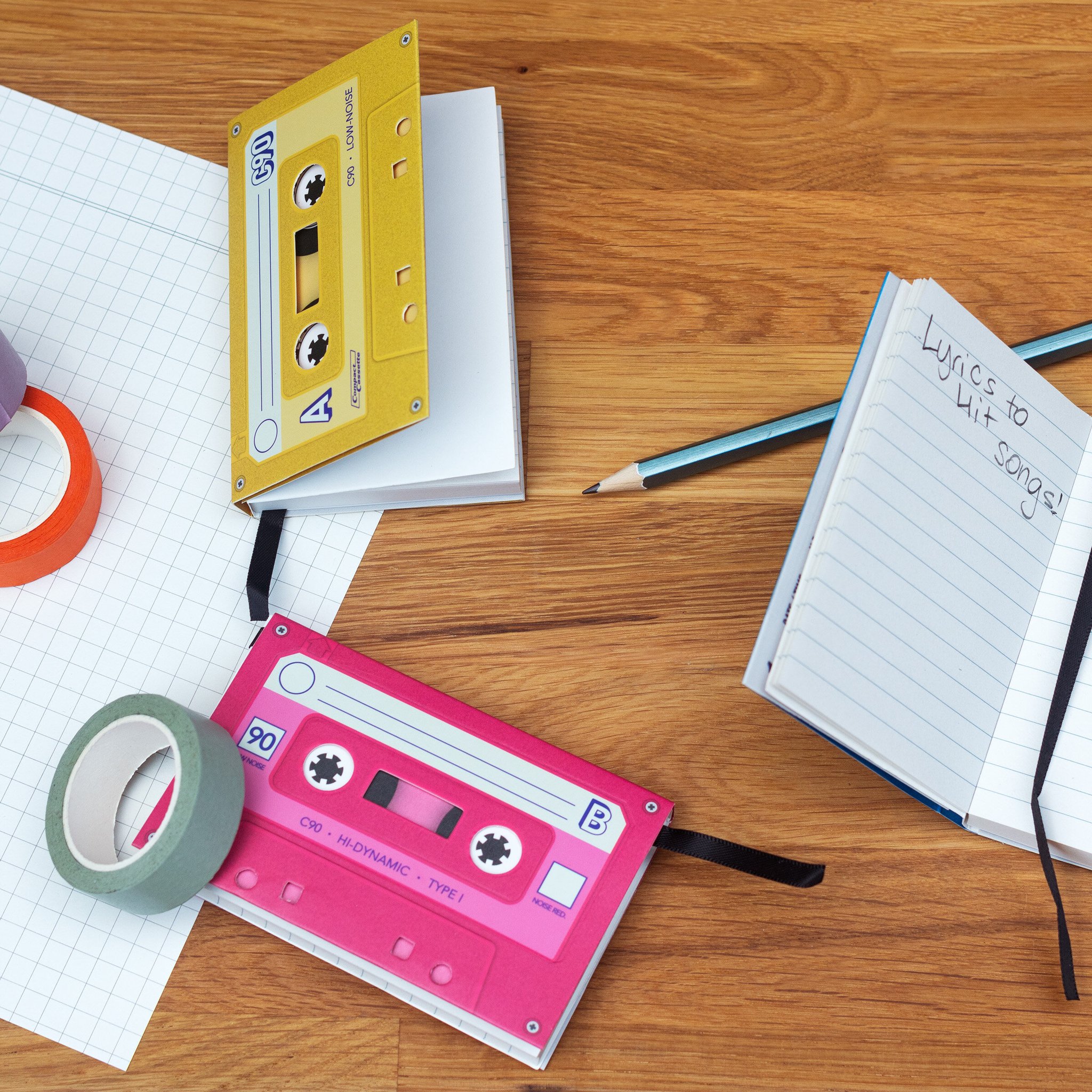 Cassette-styled notebooks on a wooden desk with pencil and tape