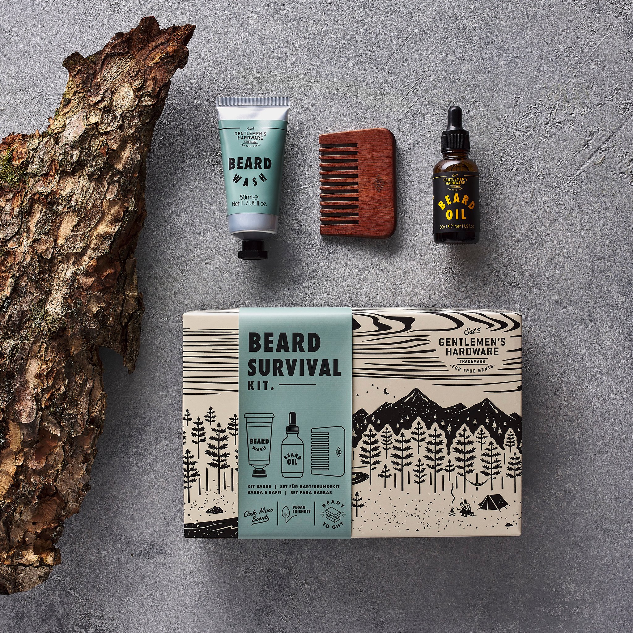 Beard Survival Kit von oben auf grauem Stein: Schachtel, Bartwasch, Holzkamm und Bartöl neben einem Stück Baumrinde