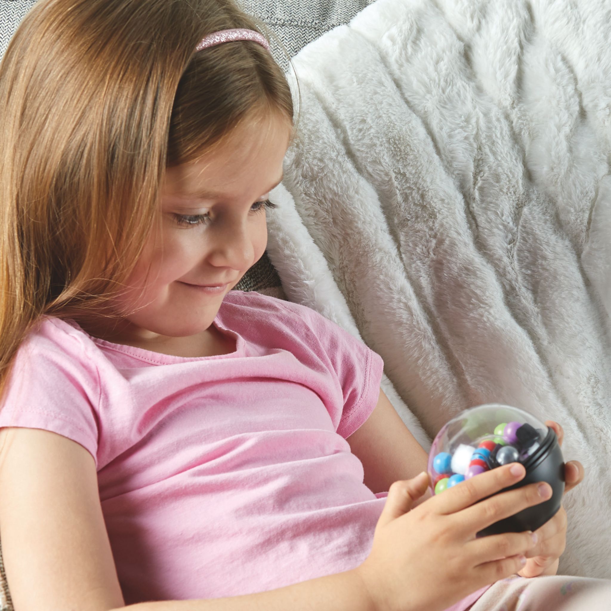Mädchen lächelt beim Spielen mit dem Scramboozle Puzzle-Ball auf dem Sofa