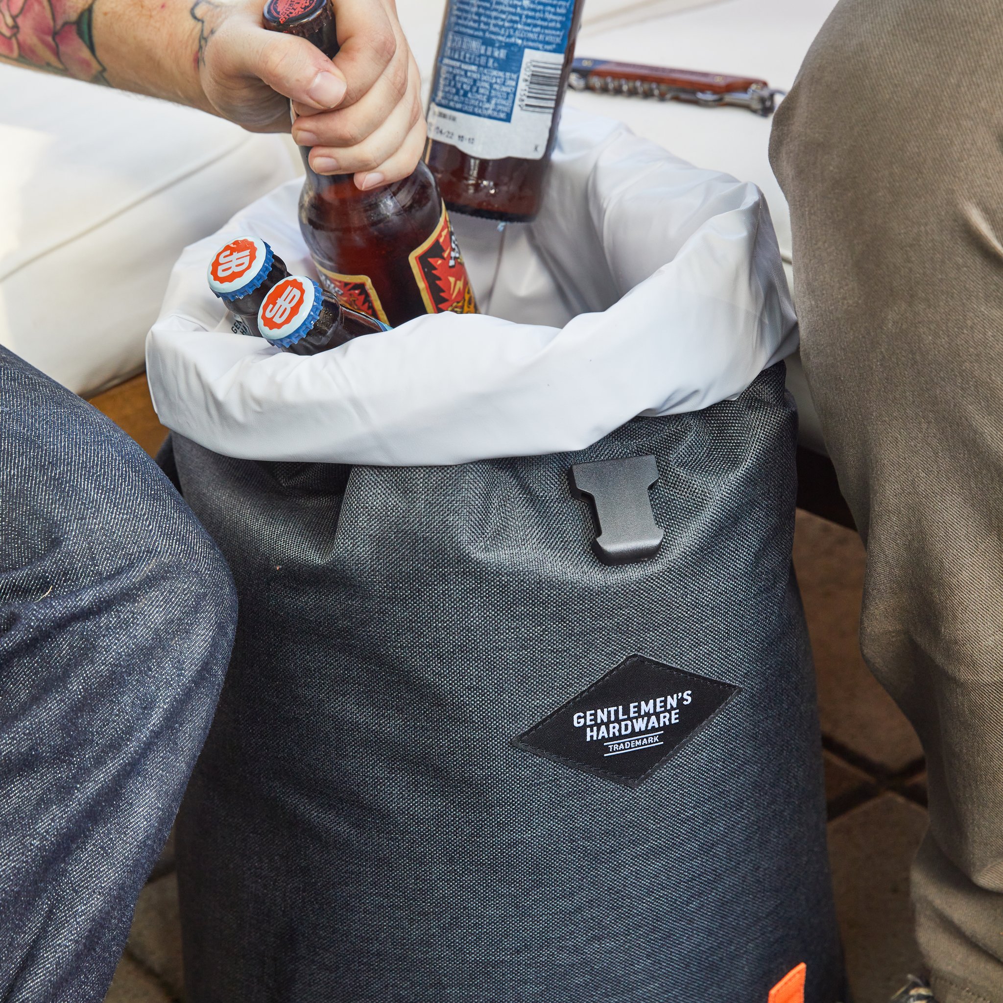 Jemand greift im Sitzen in den offenen Kühlrucksack voller Bierflaschen mit hellem Innenfutter