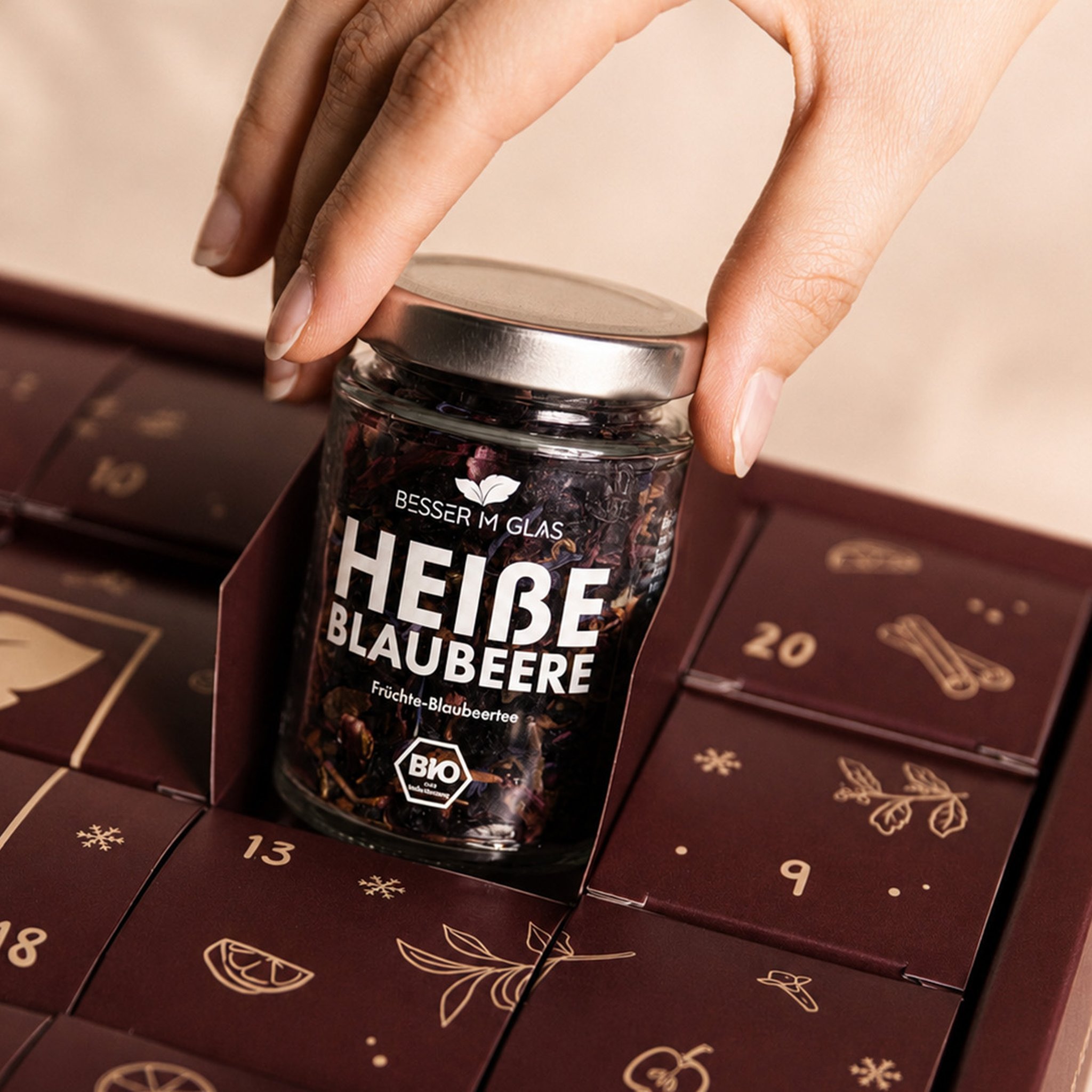 Hand nimmt ein Teeglas aus einem geöffneten Türchen des Tee- und Gewürz-Adventskalenders