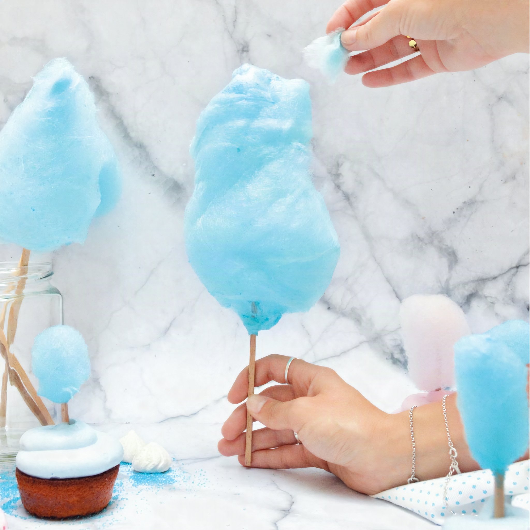 Mains façonnant de la barbe à papa bleue sur un bâtonnet au-dessus d'un cupcake