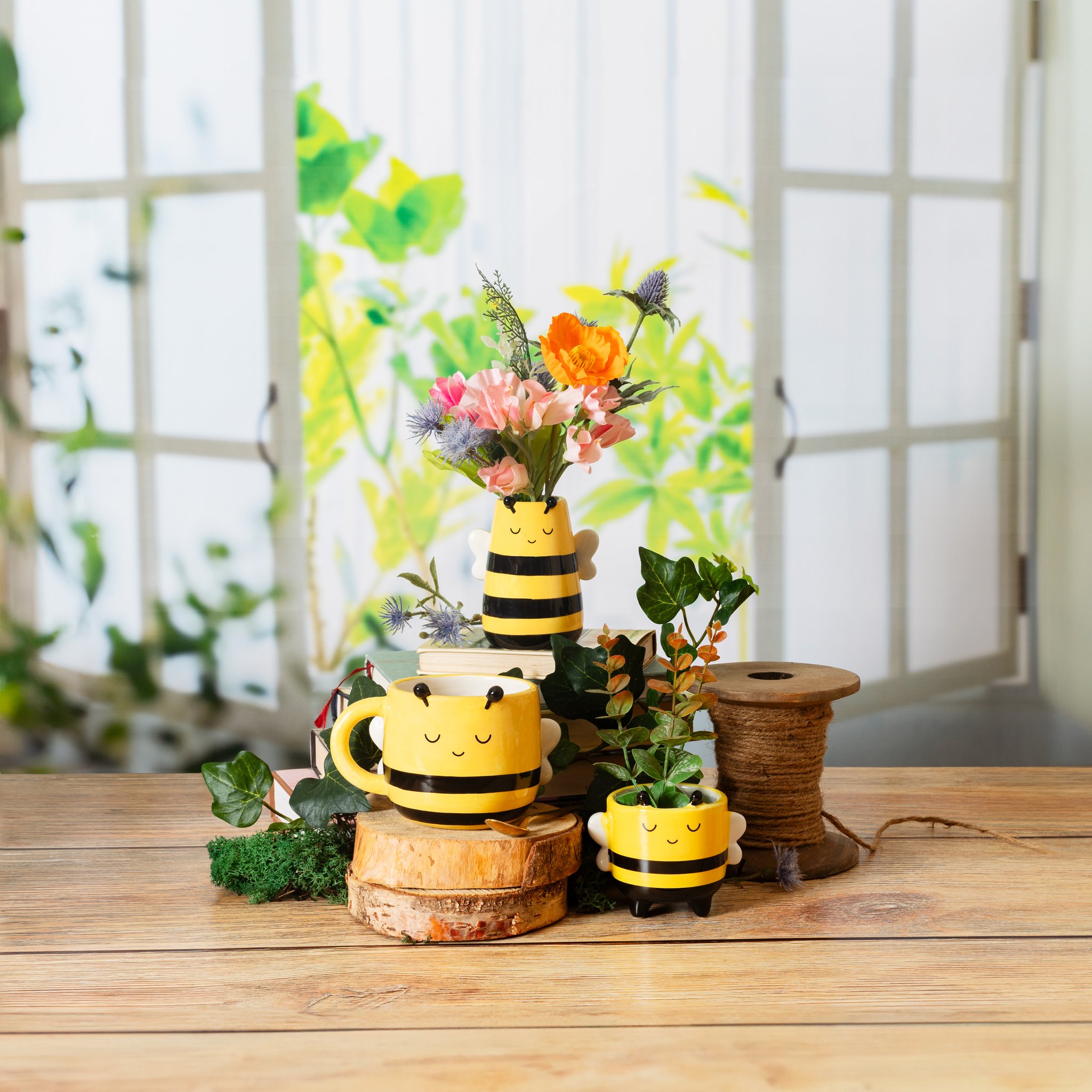 Bienenvase mit Blumen neben Bienen-Tasse und Bienen-Blumentopf auf Holz