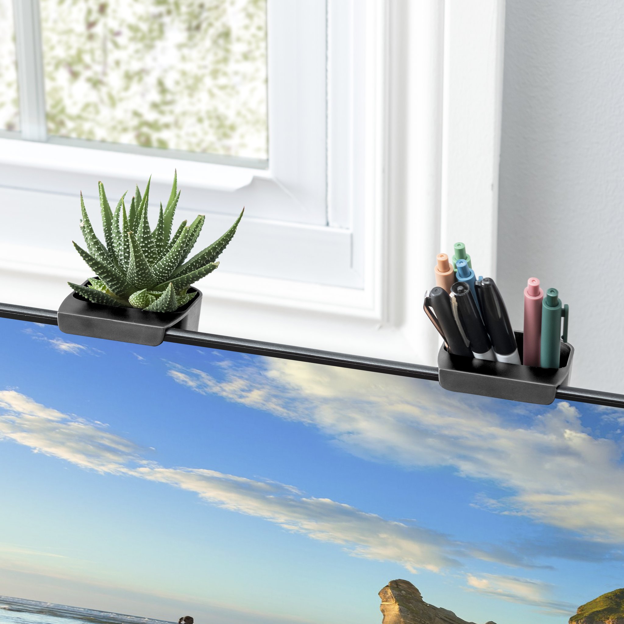Two storage pots on the monitor with plant and pens