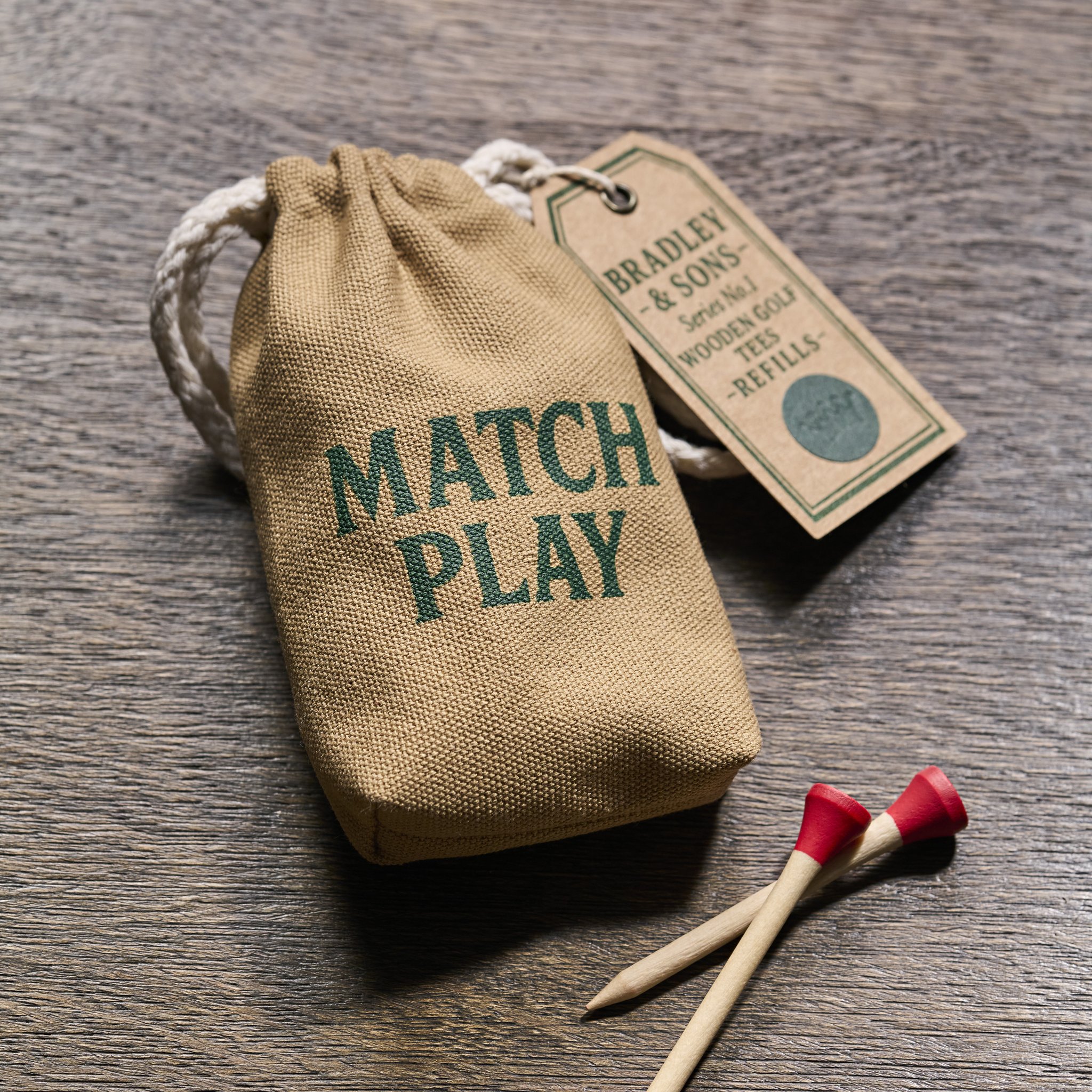 Canvas-Beutel Match Play mit Anhänger und zwei roten Birken-Tees auf dunklem Eichenholz