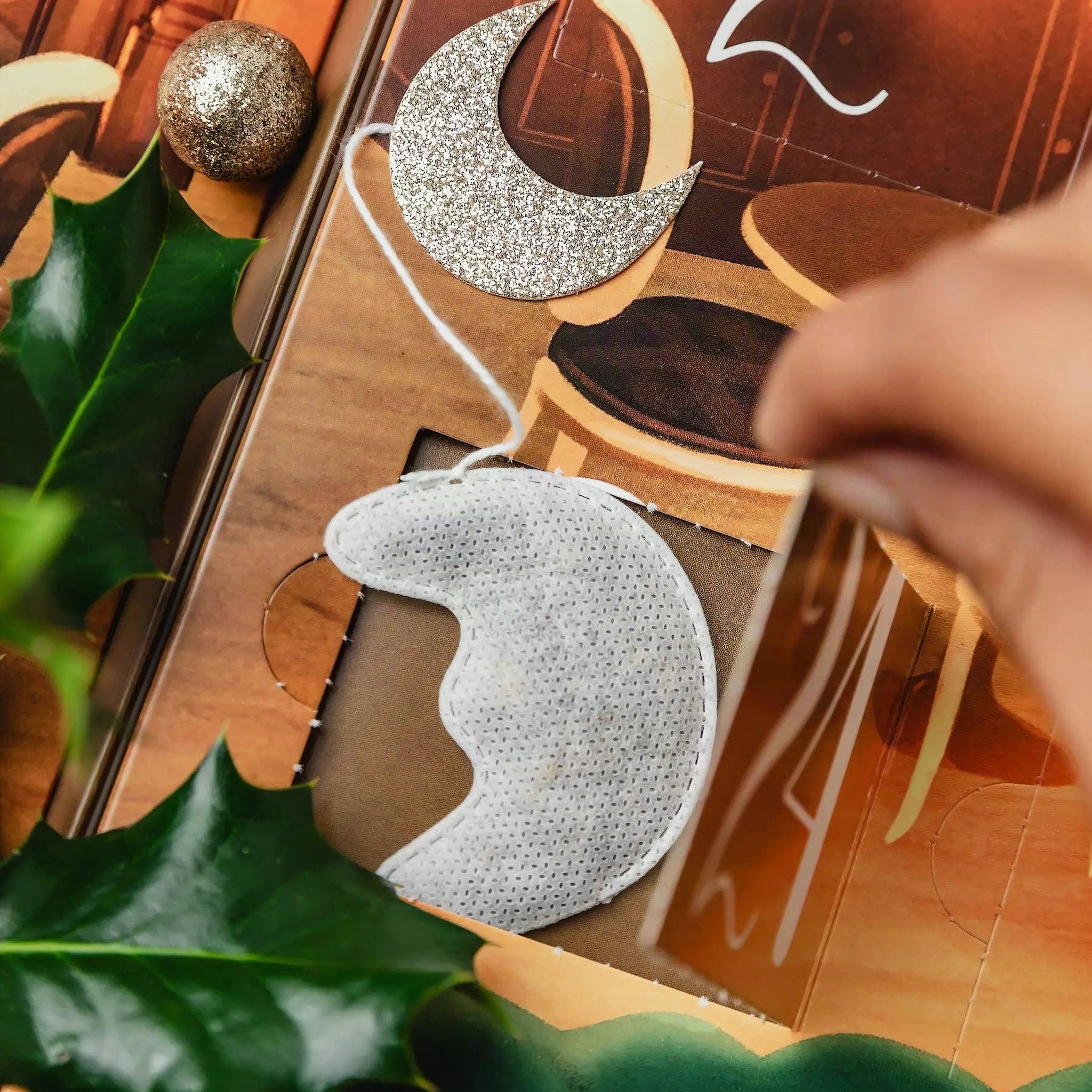 Una mano estrae una bustina a forma di luna da una finestrella aperta del calendario dell'Avvento