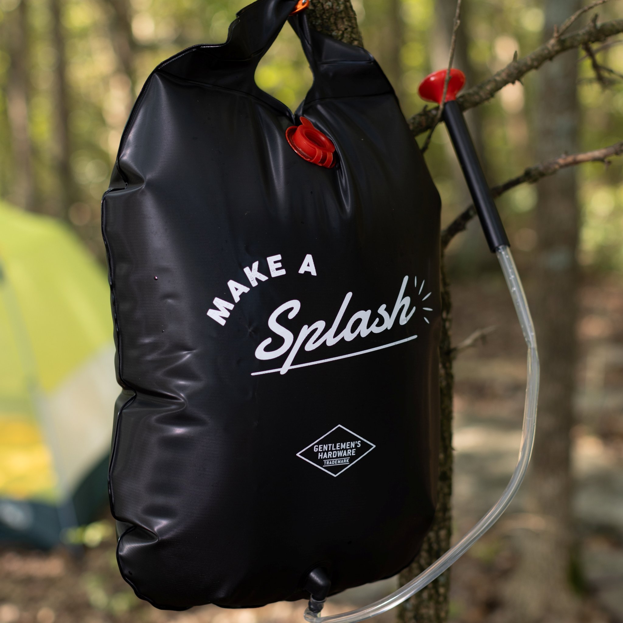 Close-up of the black portable solar shower bag on a branch, its clear hose hanging down the side