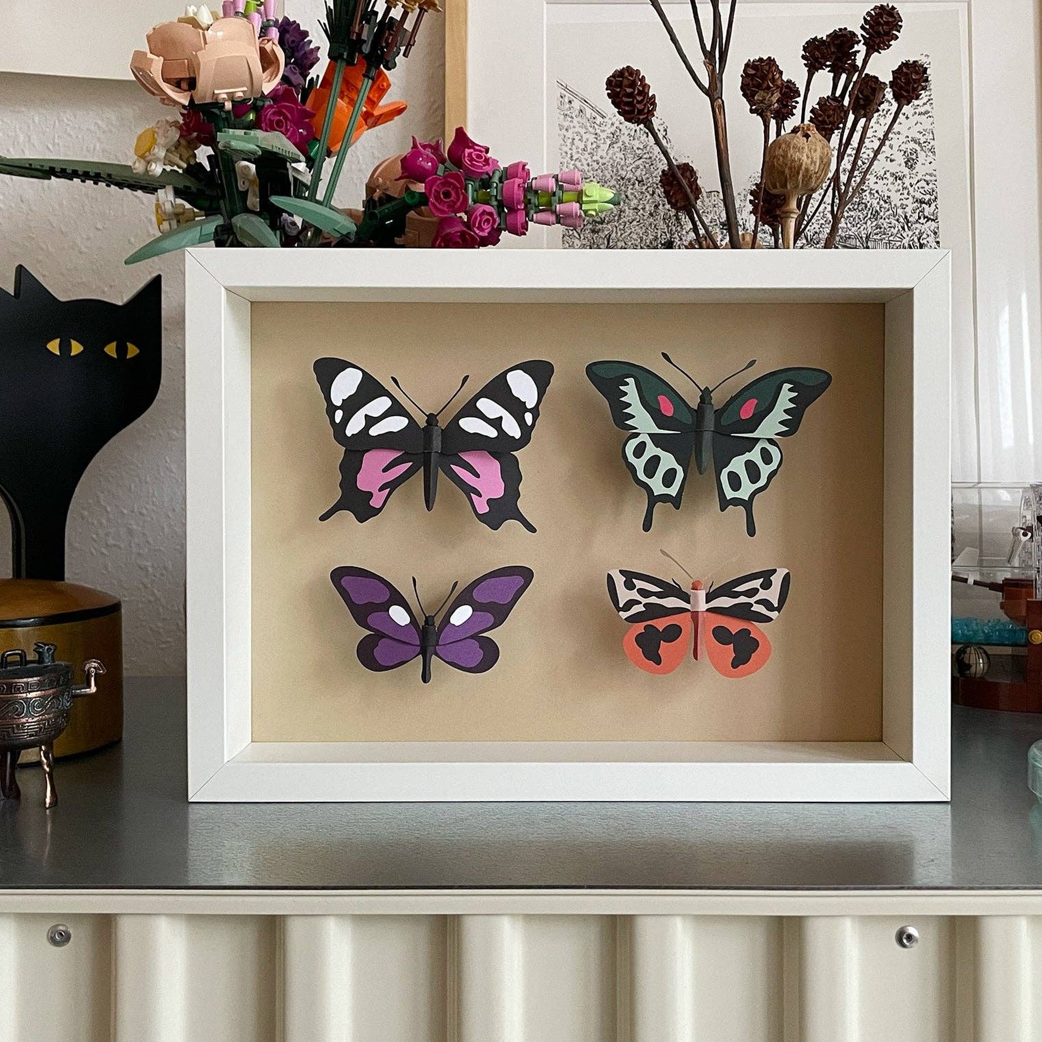 Gefaltete Papierschmetterlinge im Bilderrahmen auf einem Regal