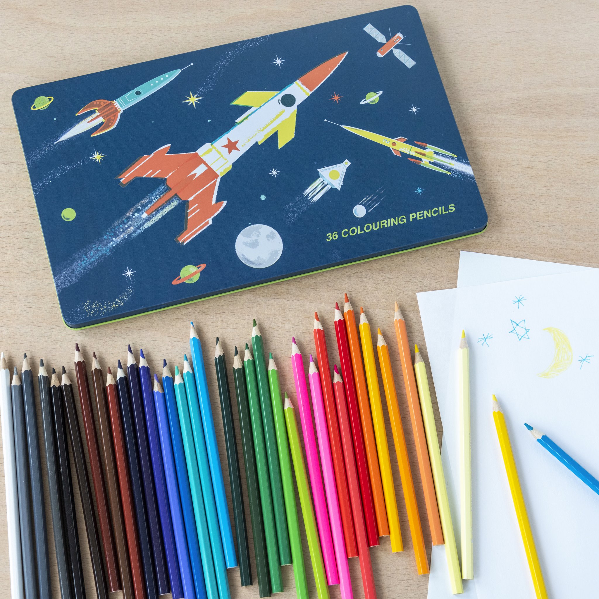 Space Age colouring pencils in the tin with rocket motif next to a child's drawing