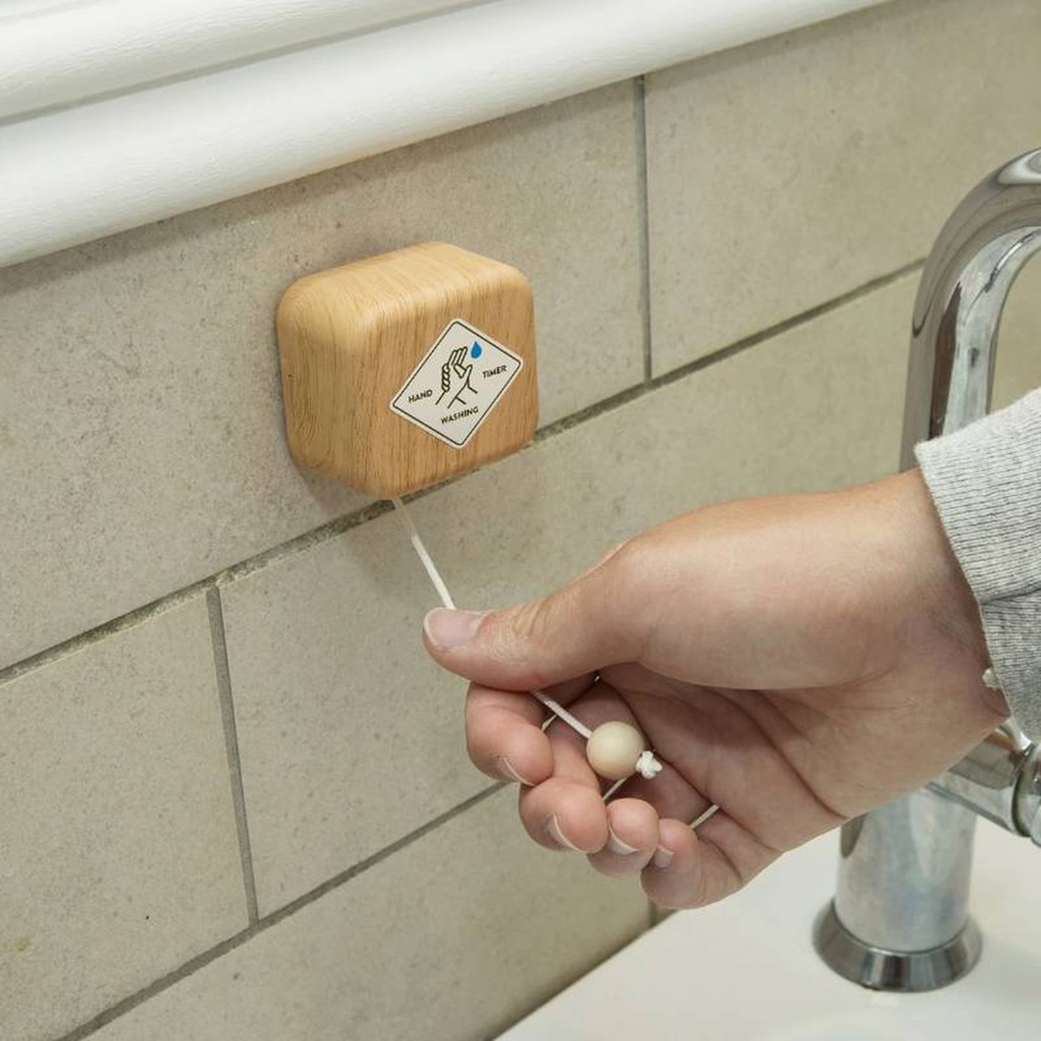 Hand zieht die Kugel des Händewasch-Timers an der Wand neben dem Waschbecken