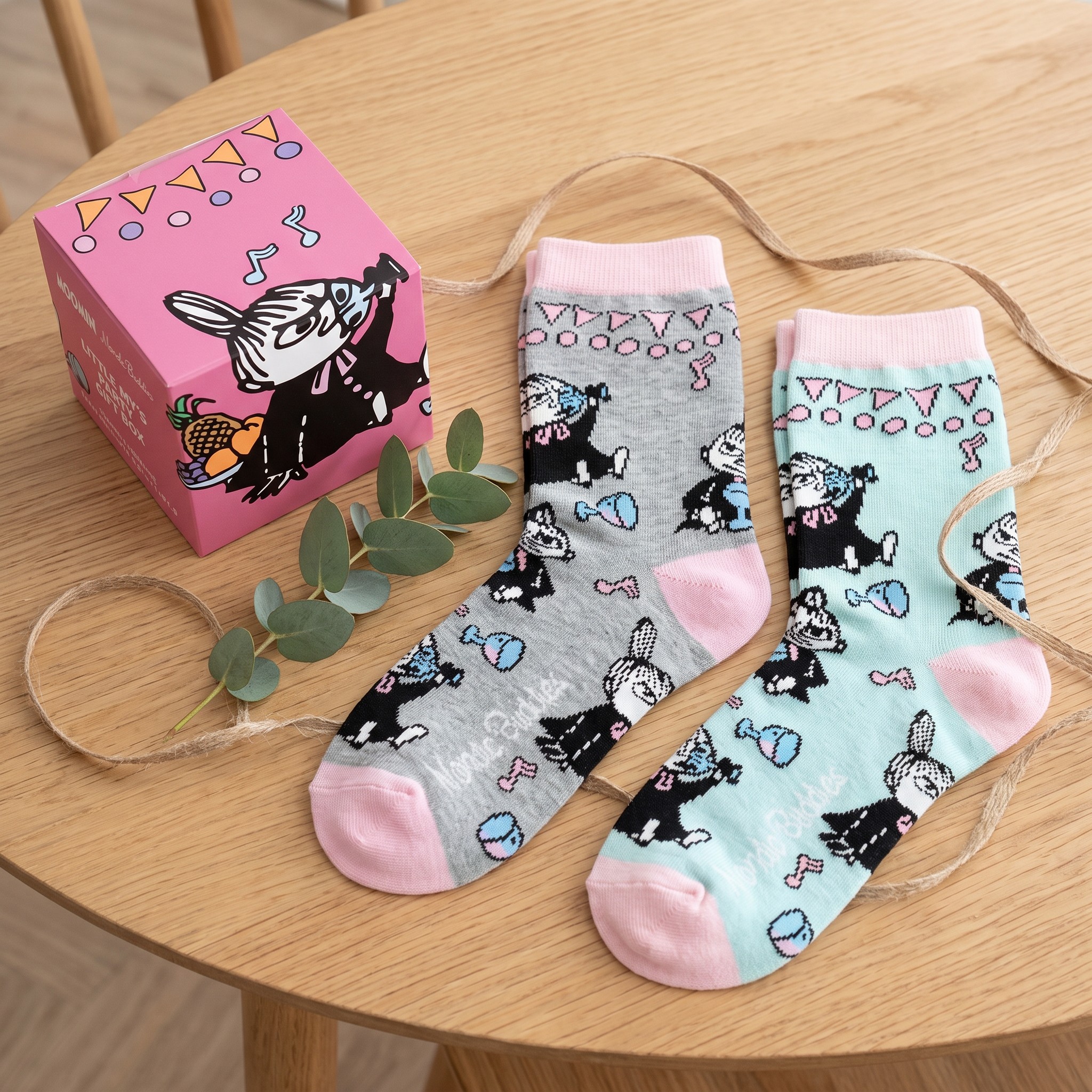 Both pairs of Moomin socks next to the pink gift box on a wooden table