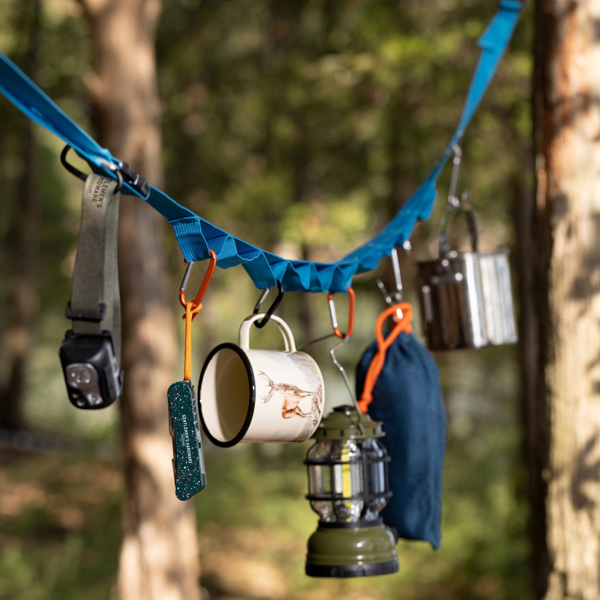 Woodland scene with the blue hanging strap carrying a headtorch, mug, lantern and a dark blue pouch