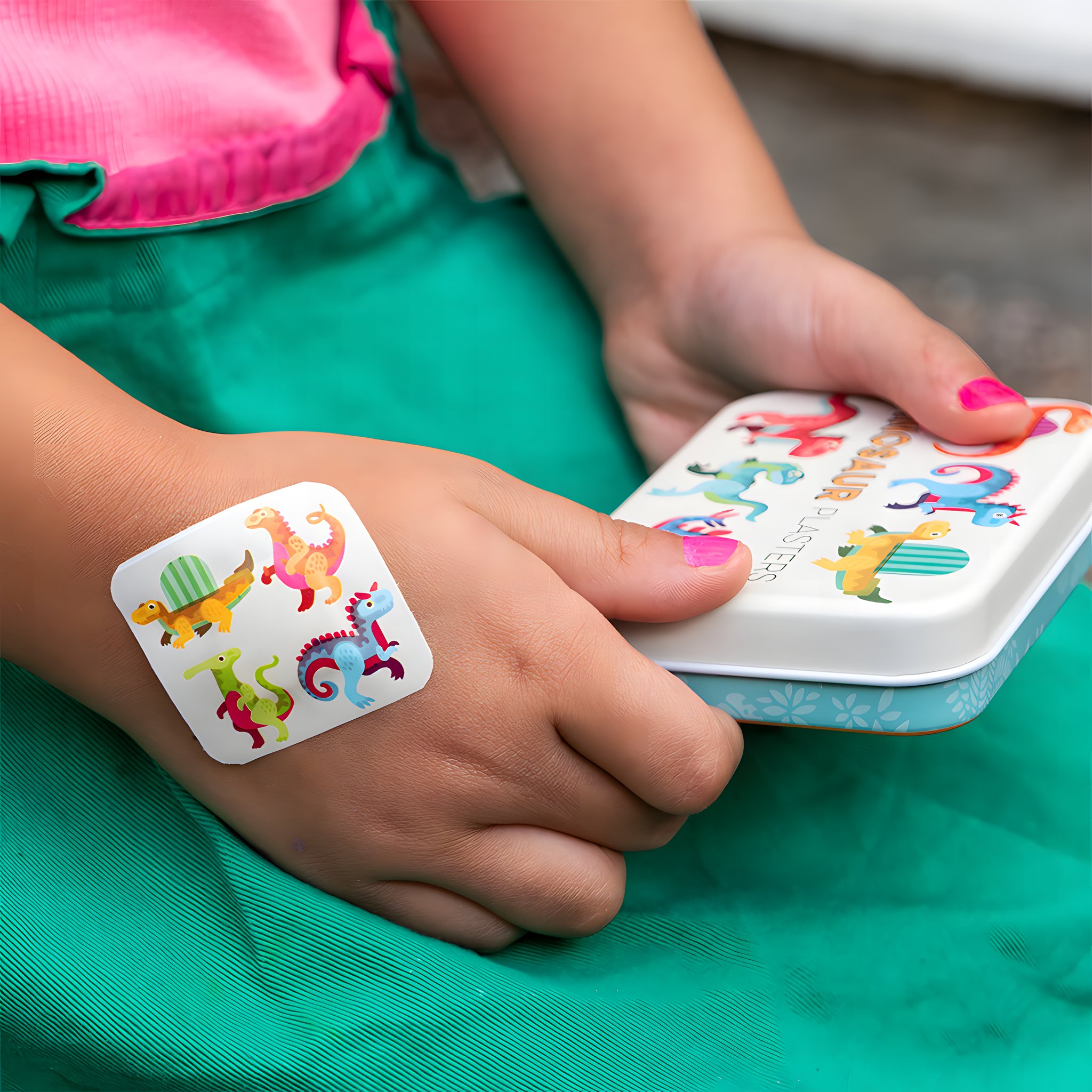 Kinderhand mit Dino-Pflaster, daneben die Metalldose der Baby-Dinos Kinderpflaster