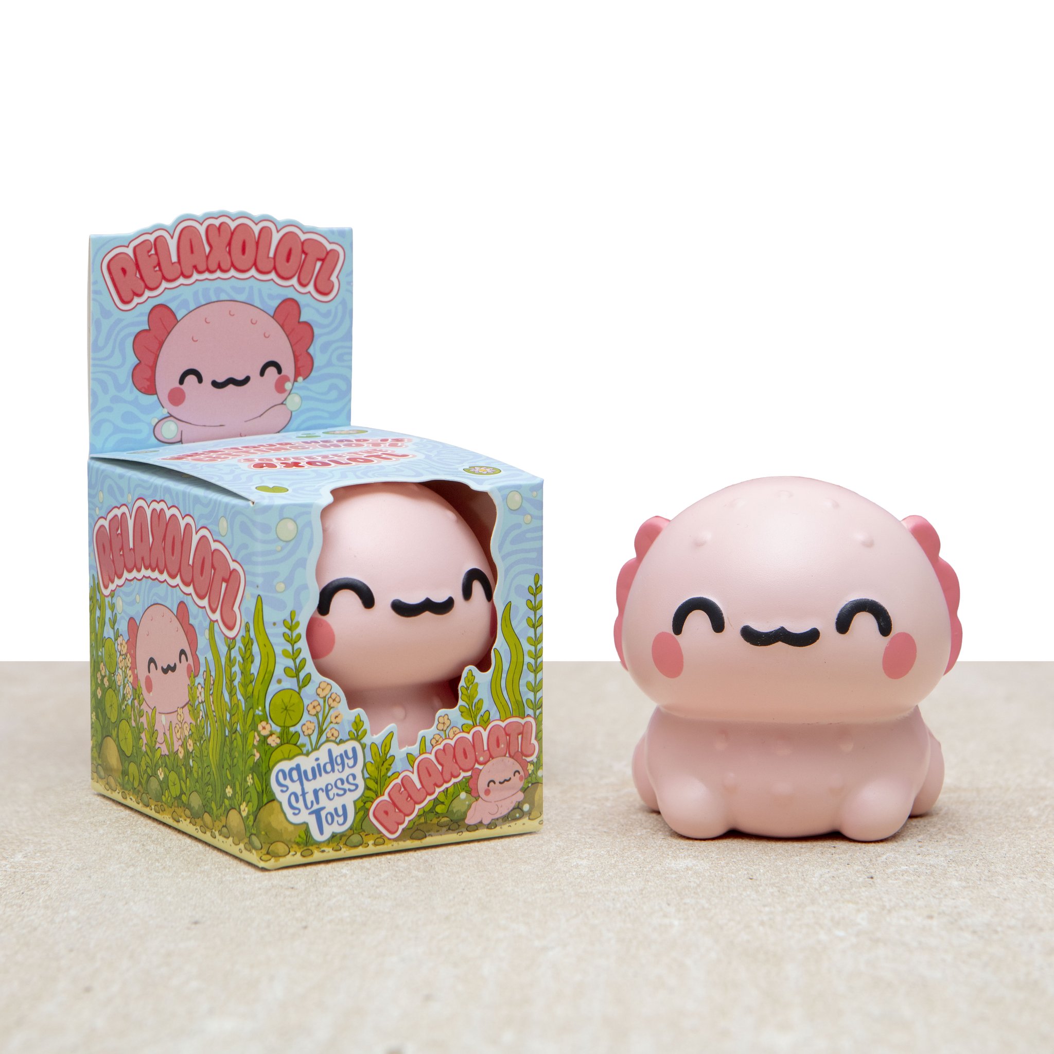 Relaxolotl Axolotl Squishy in Rosa neben seiner Verpackung mit Sichtfenster auf hellem Tisch