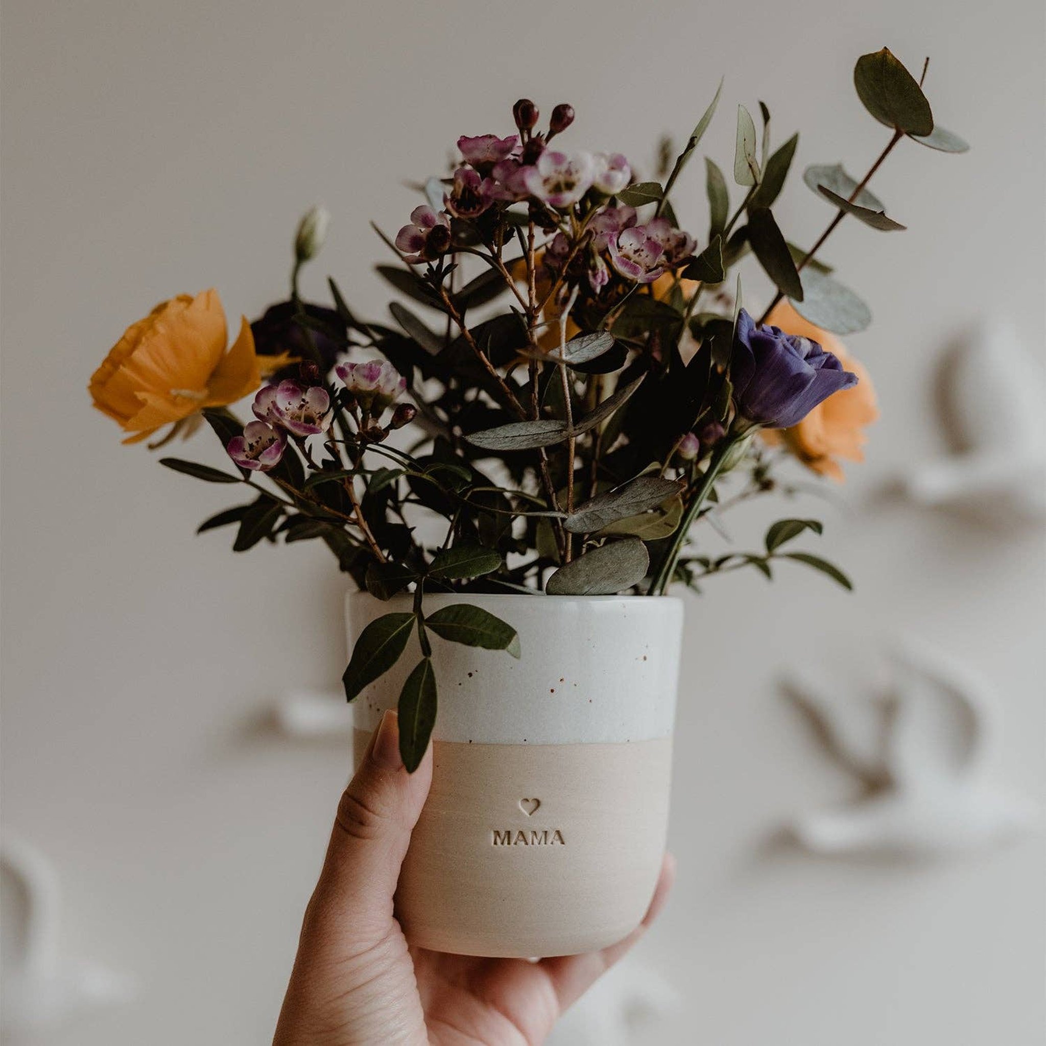 Hand hält den Becher Mama als kleine Vase mit einem bunten Blumenstrauss
