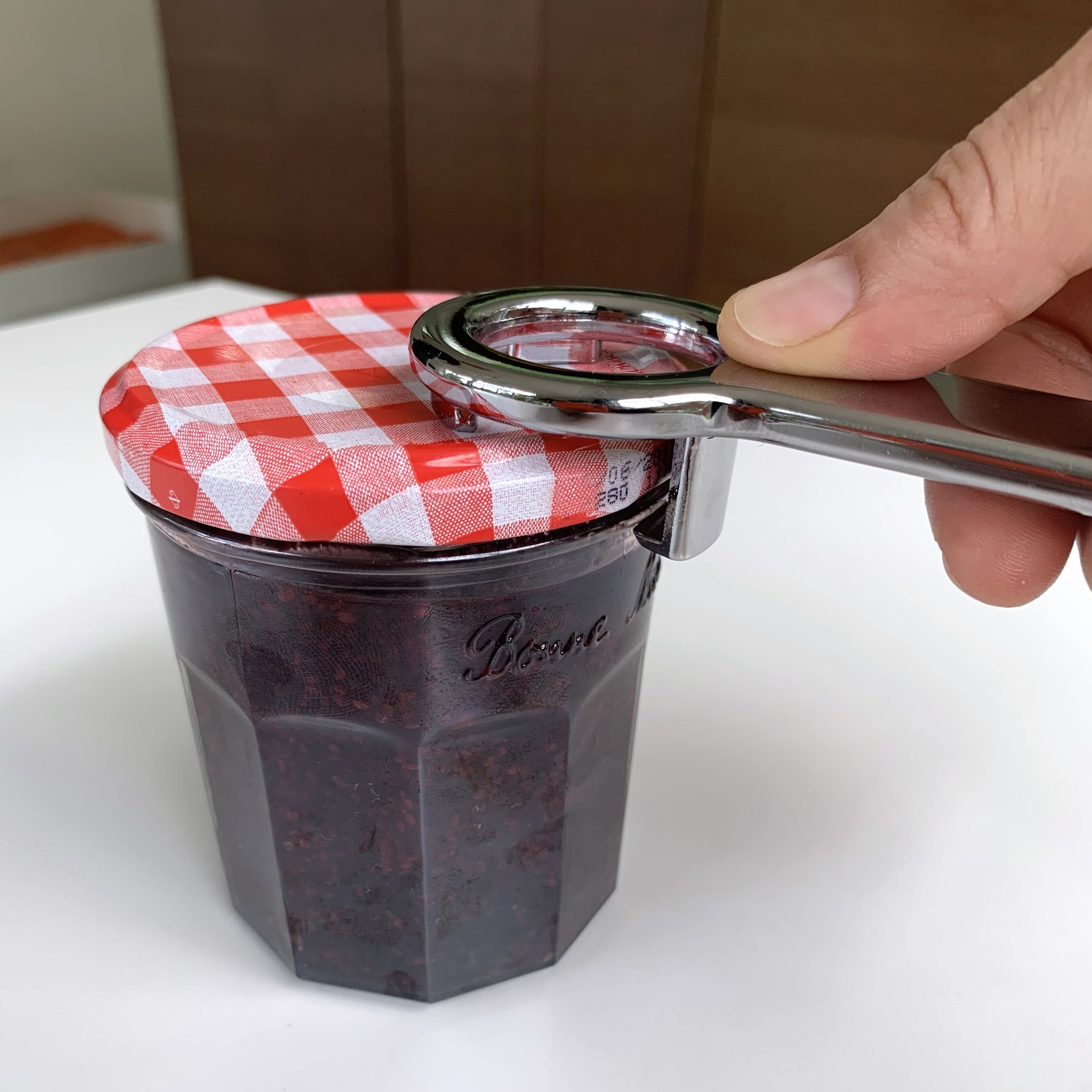 Hand setzt den Öffner am Deckel des Konfitürenglases an