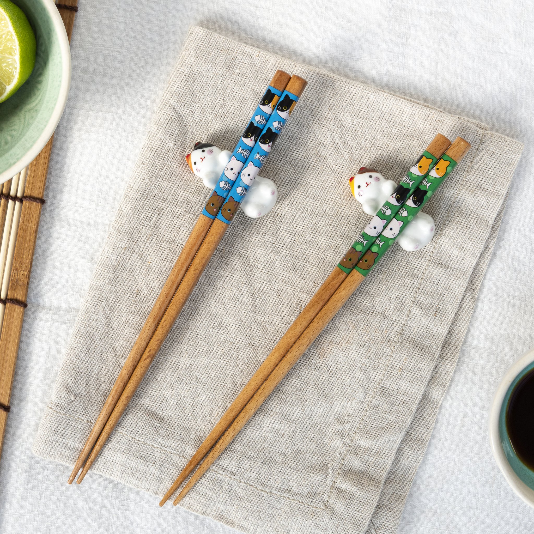Bamboo chopsticks with blue and green cat pattern resting on the ceramic cats on linen