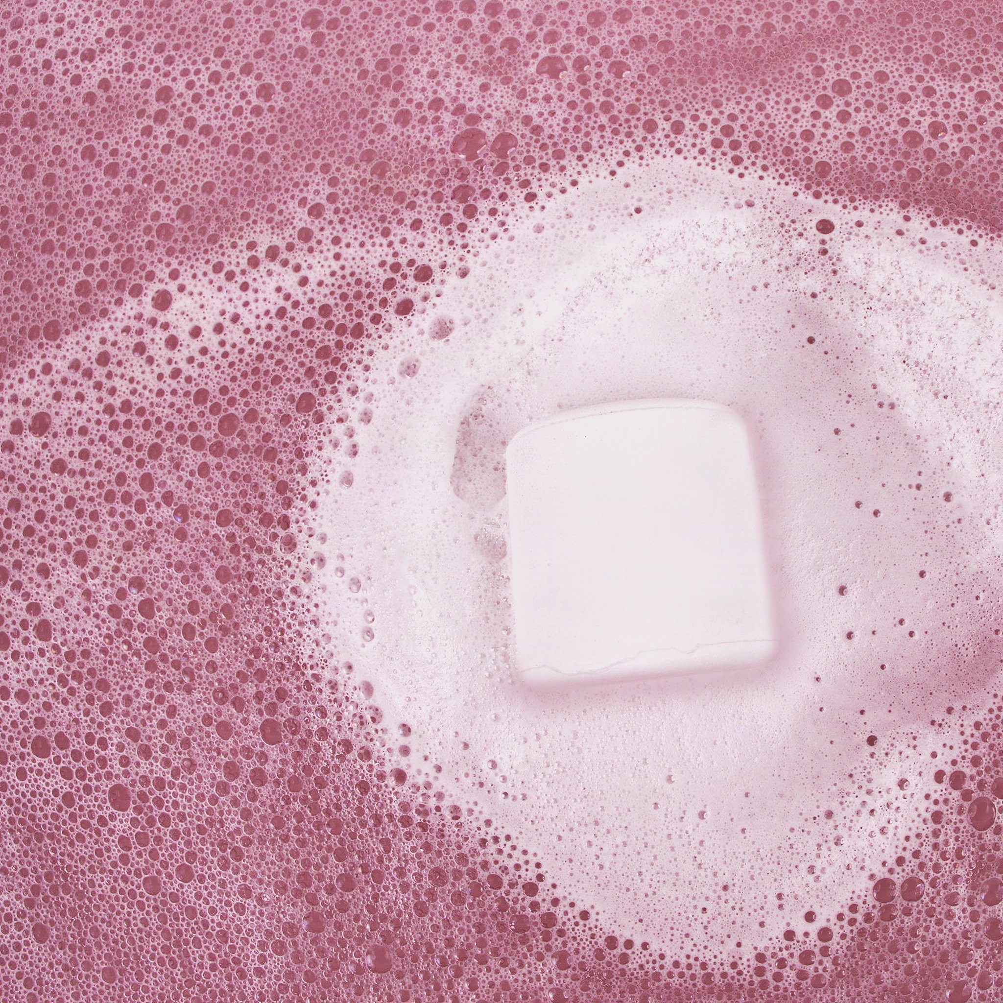 White marshmallow bath bomb dissolving in white foam in pink bath water
