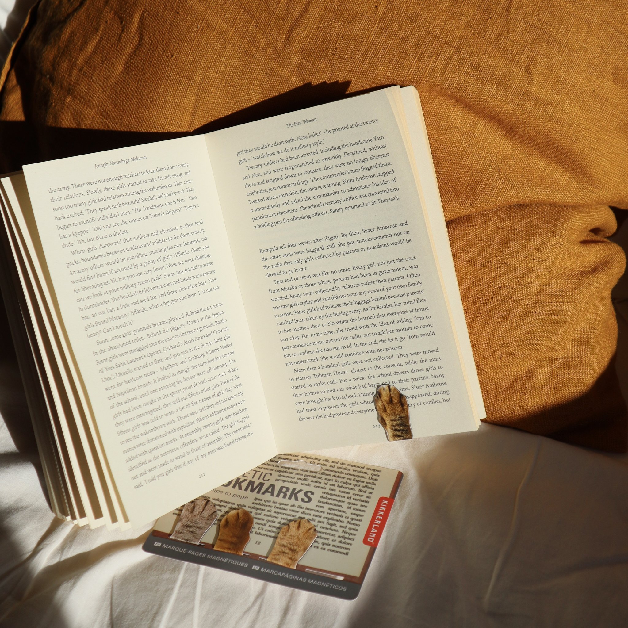 Aufgeschlagenes Buch mit Katzenpfoten-Lesezeichen und der Verpackung auf dem Bett