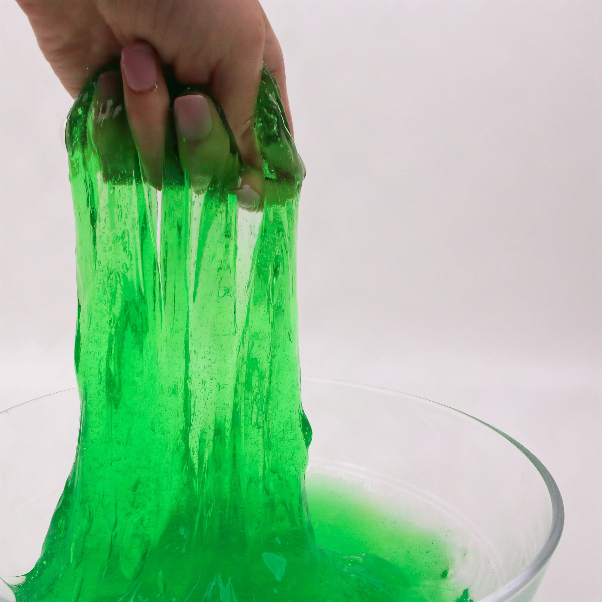 Hand pulling green slime from a glass bowl