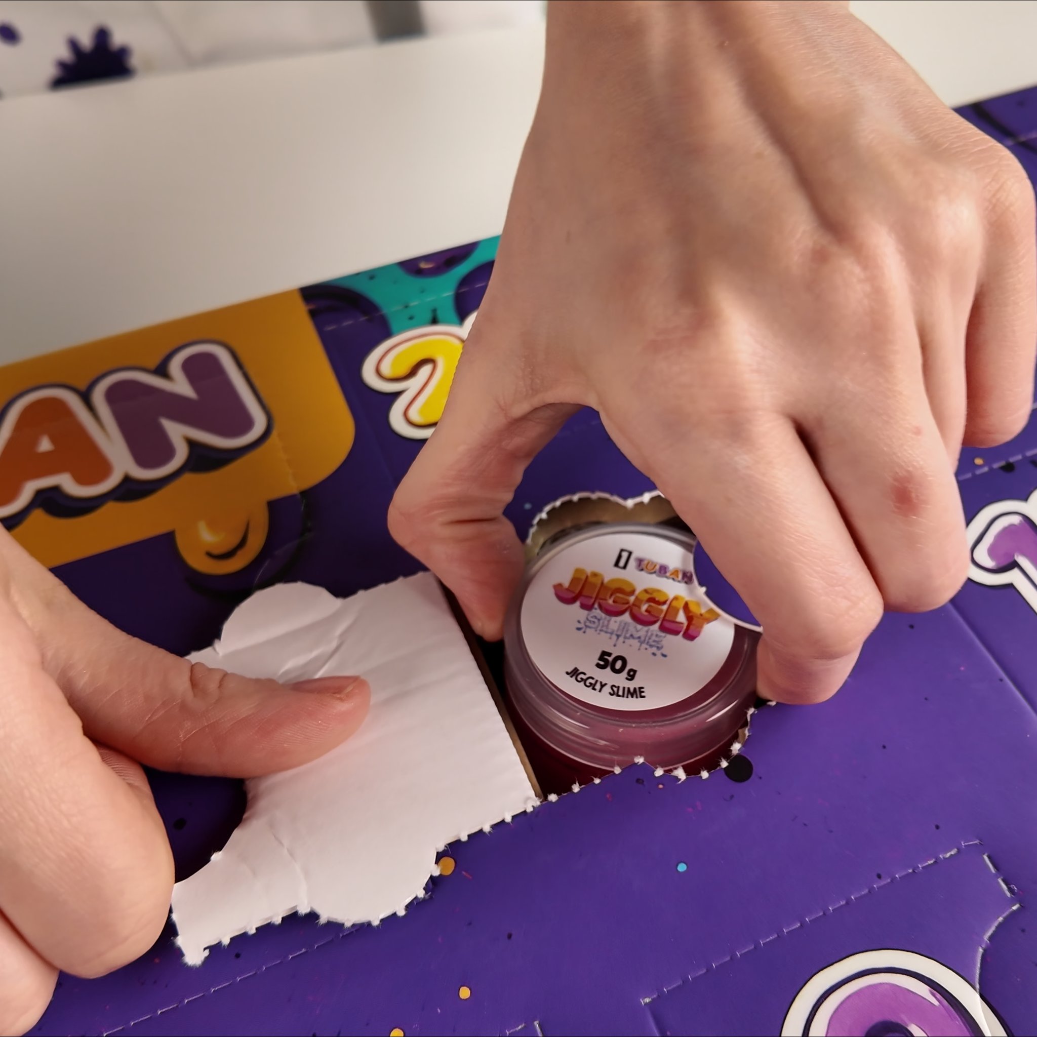 Hände öffnen ein Türchen des Slime-Adventskalenders mit einem Döschen Jiggly Slime