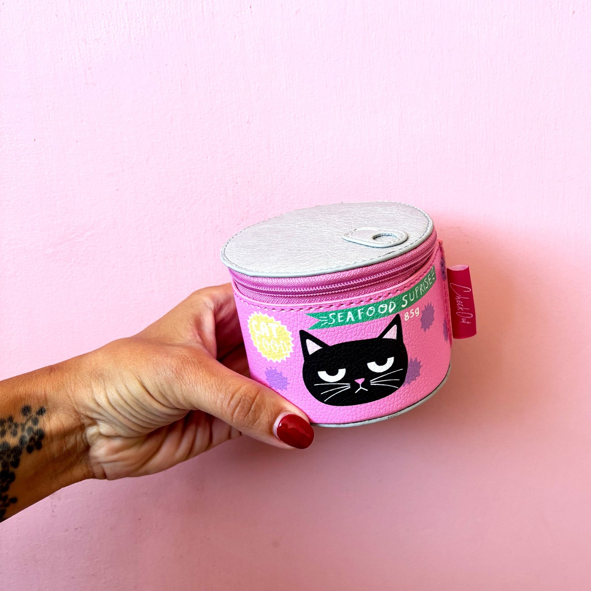 Cat food tin case with a grumpy black cat held against a pink wall