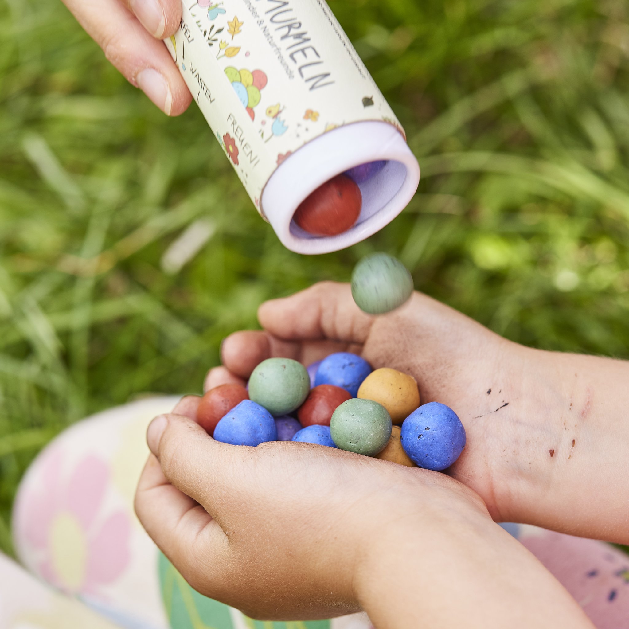 Kinderhände fangen bunte Blumenmurmeln auf, die aus der Dose geschüttet werden