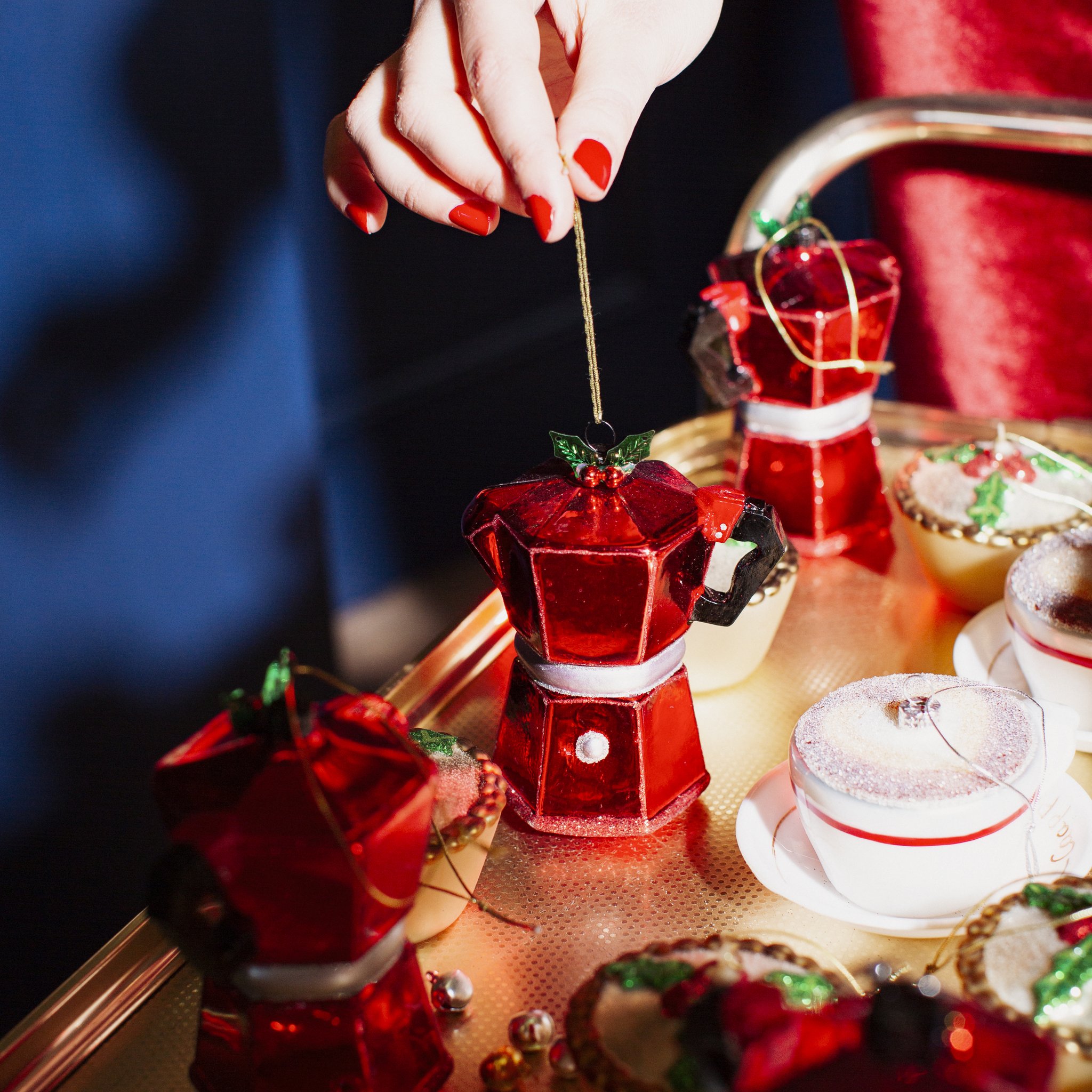 Hand hält die Kaffeekannen-Weihnachtsdekoration vor rotem Samt