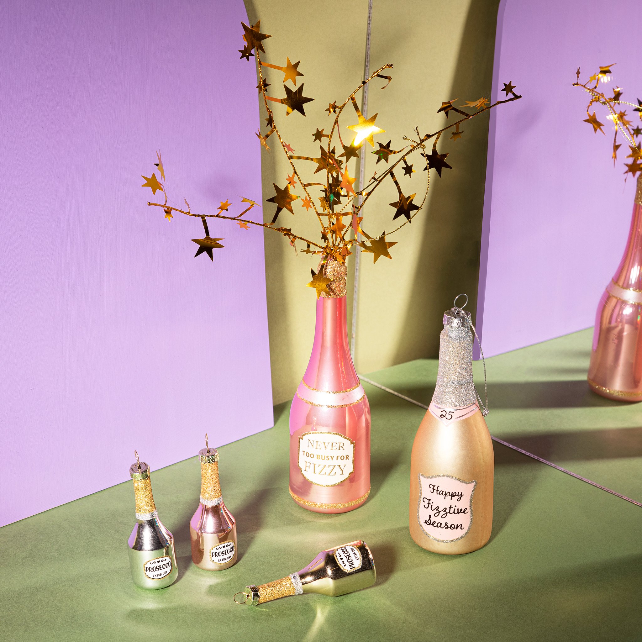 Set de décorations de Noël prosecco devant des arches violettes avec grands ornements bouteilles et branches étoilées