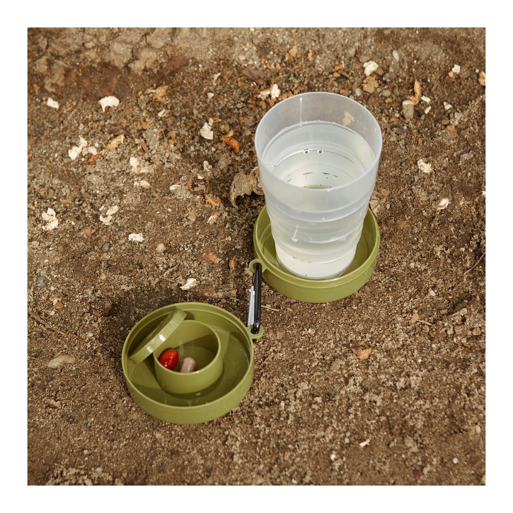 Bicchiere pieghevole con scomparto pillole in uso a terra, pieno d'acqua