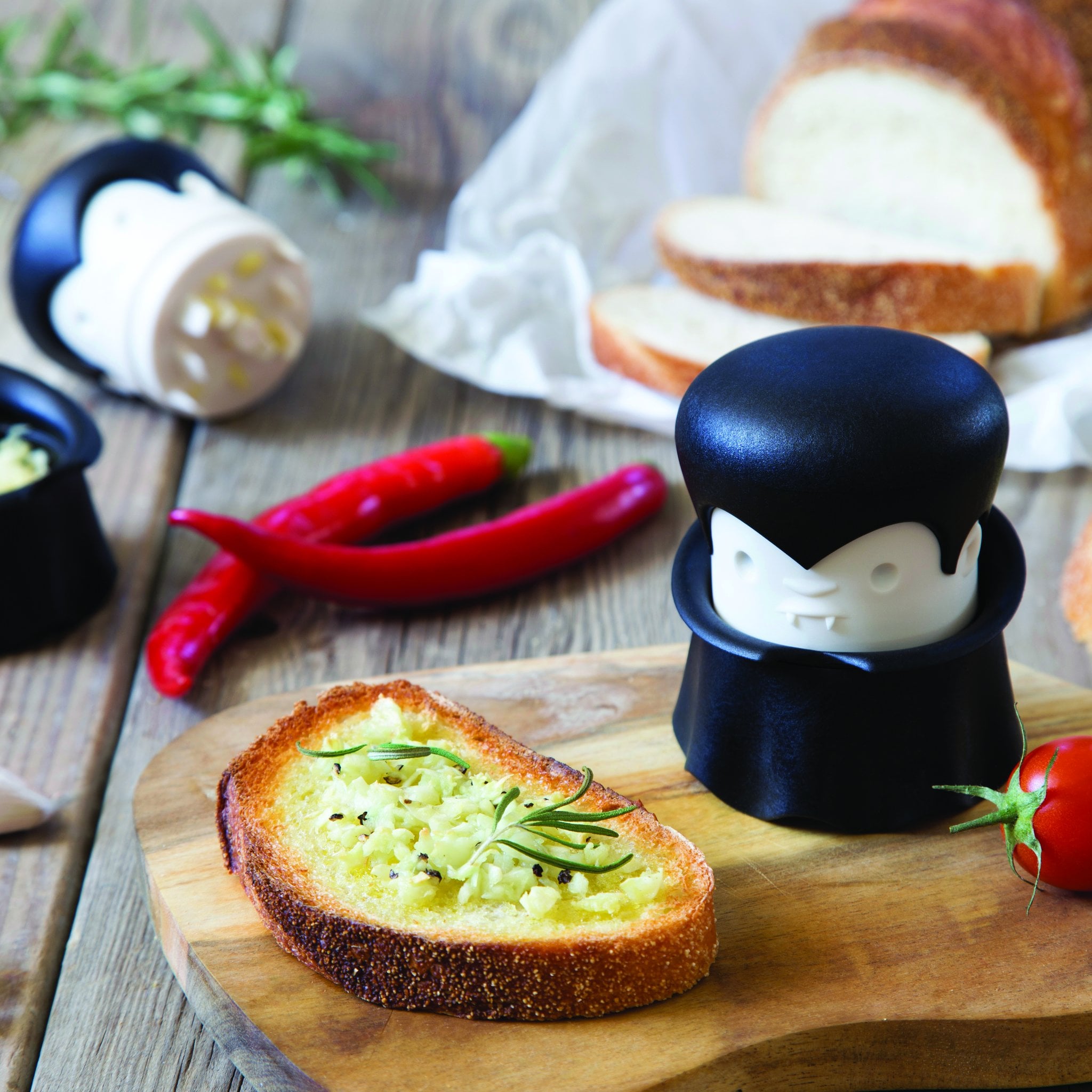 Gracula Knoblauchpresse auf dem Küchenbrett neben geröstetem Brot mit Knoblauchbutter