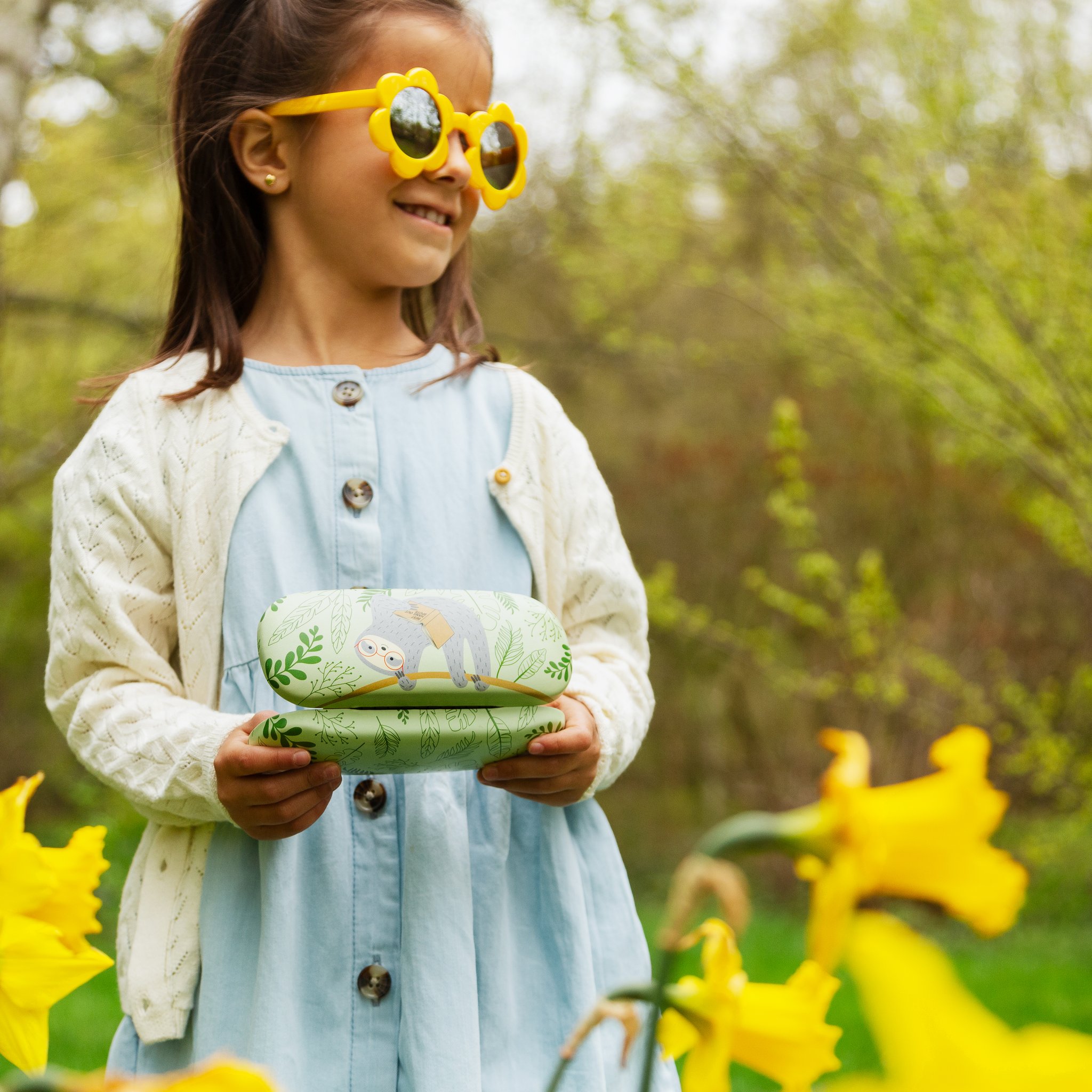 Mädchen mit Sonnenbrille hält das Faultier Brillenetui im Garten