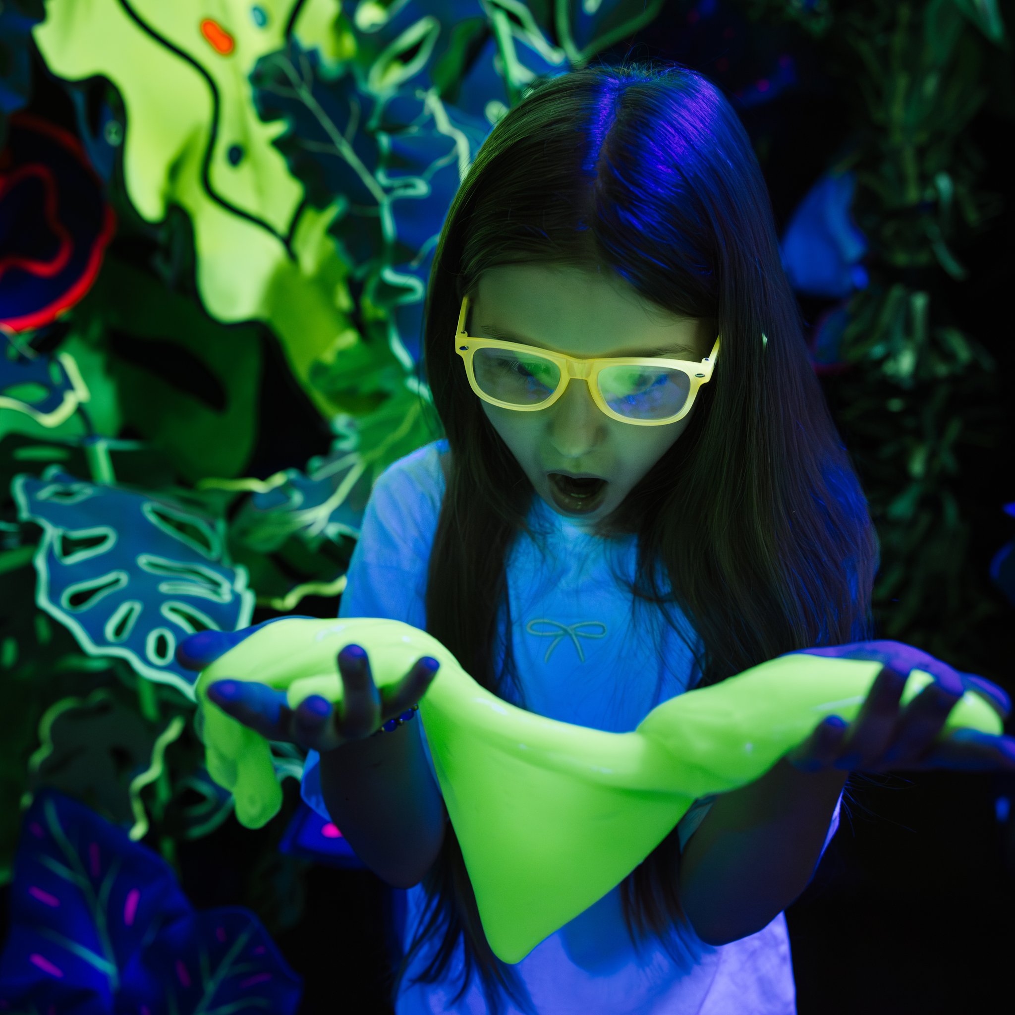 Ragazza stupita dallo Jiggly Slime verde che brilla sotto la luce UV