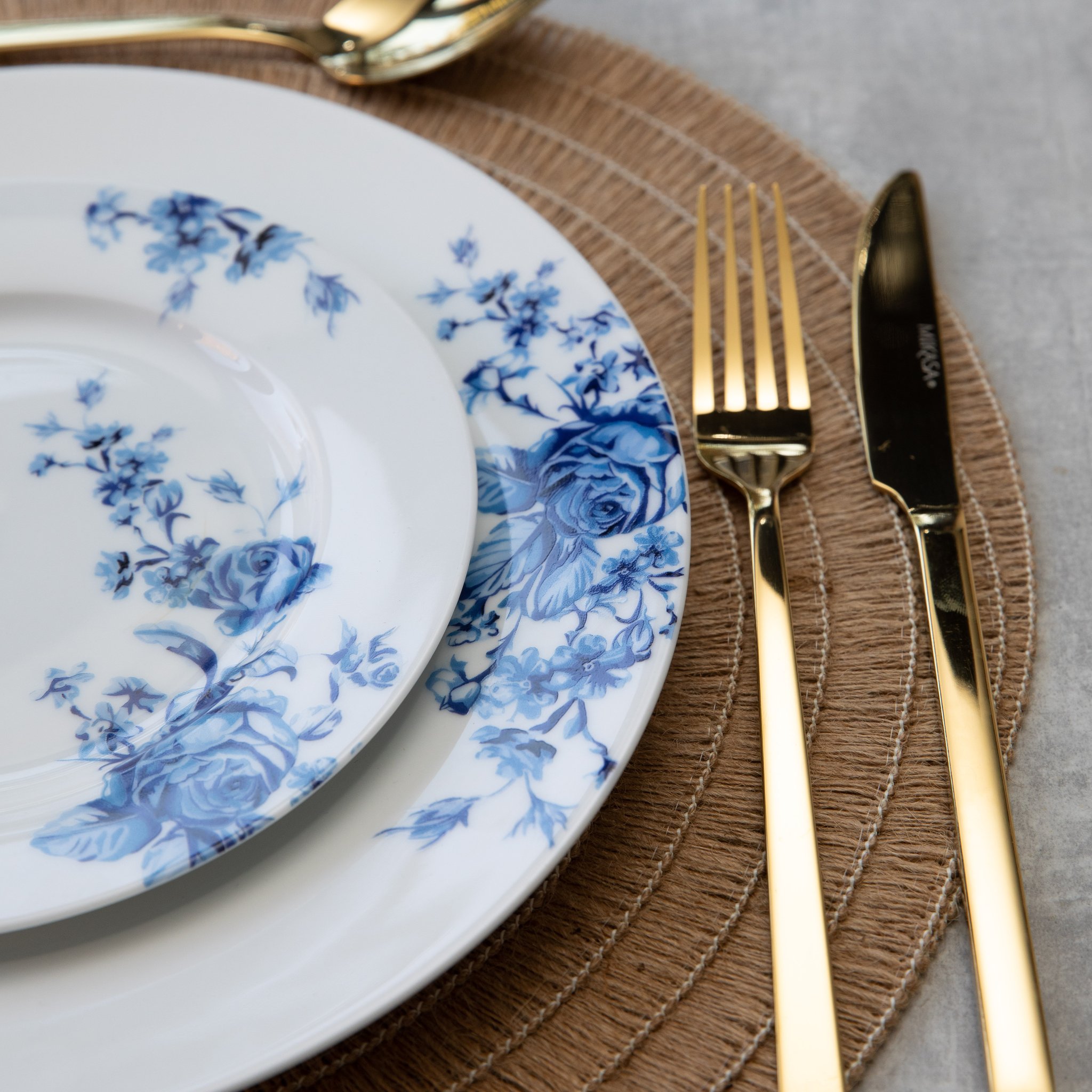 Goldbesteck neben Porzellantellern mit blauen Blumen auf geflochtenem Platzset