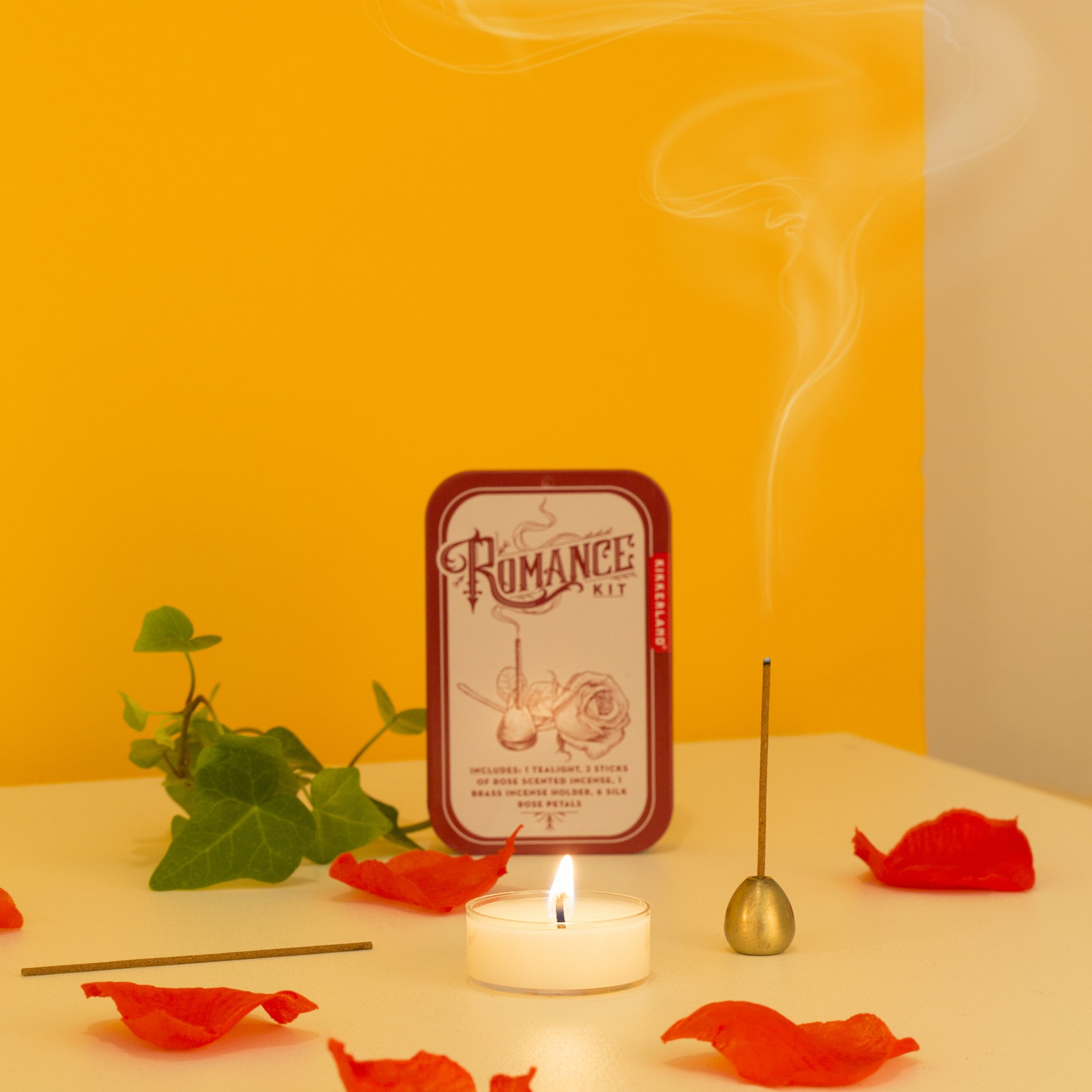 Romance kit with tin, incense, tealight and rose petals against a yellow background